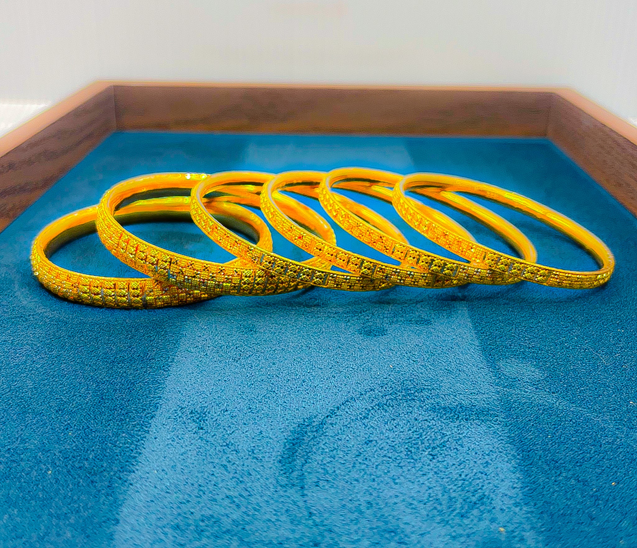 Gloved hand holding a 6-piece 22k gold bangle set with engraved pattern