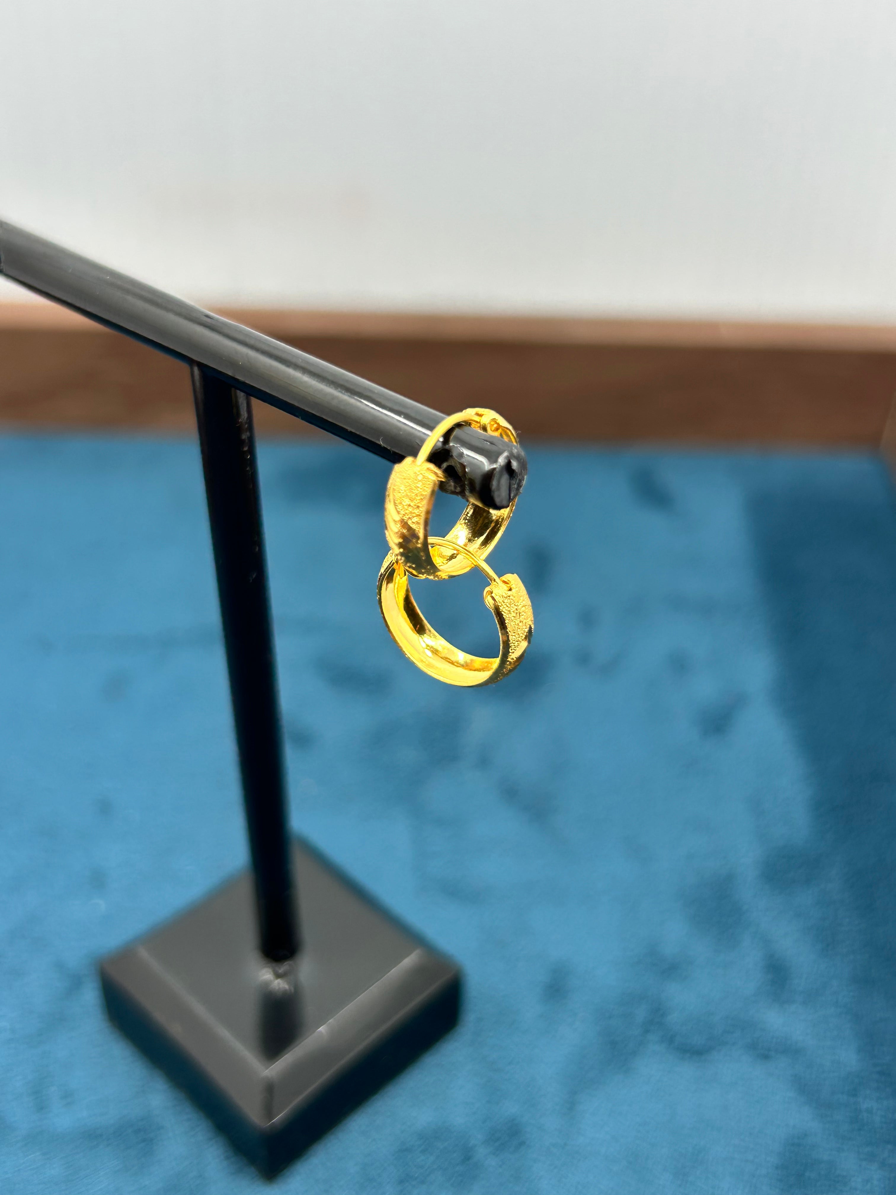Gold double hoop drop earrings on a black display stand against a blue fabric background.”