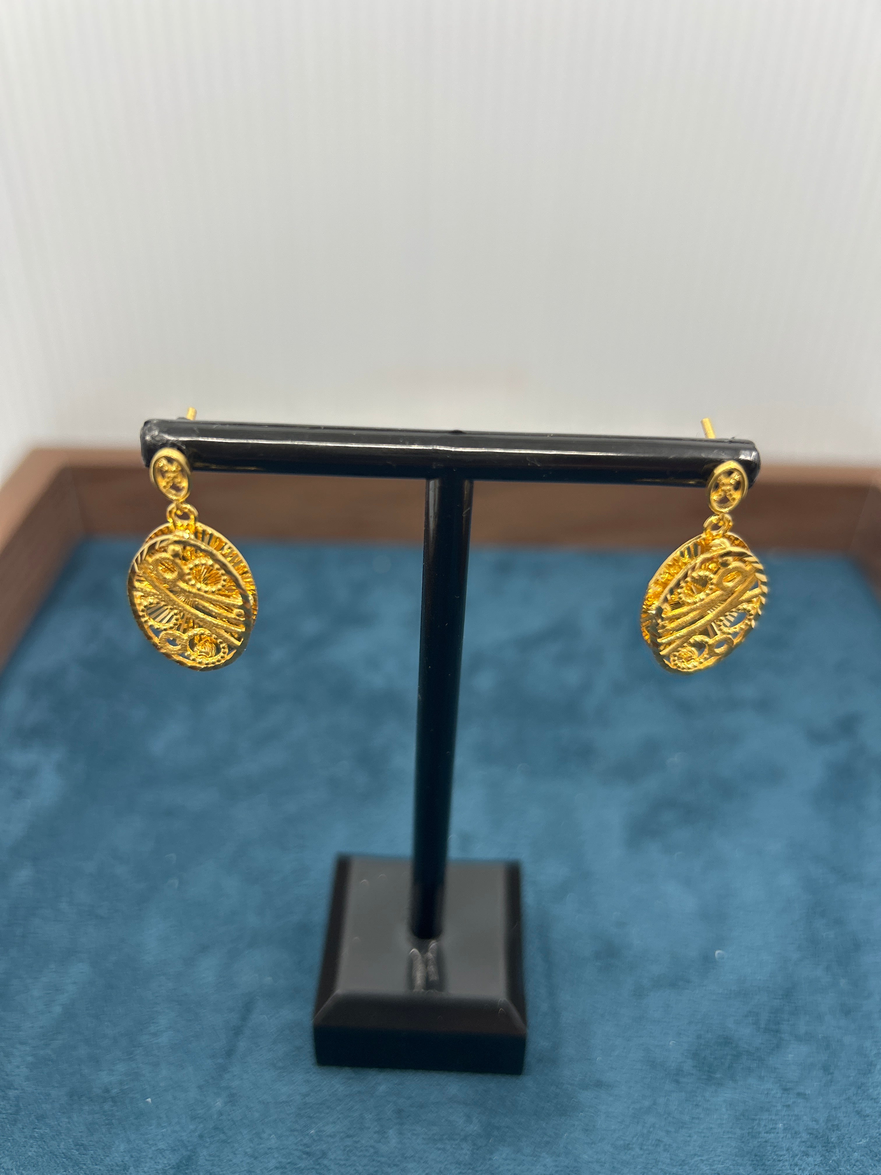 Gold earrings on a black stand against a blue background