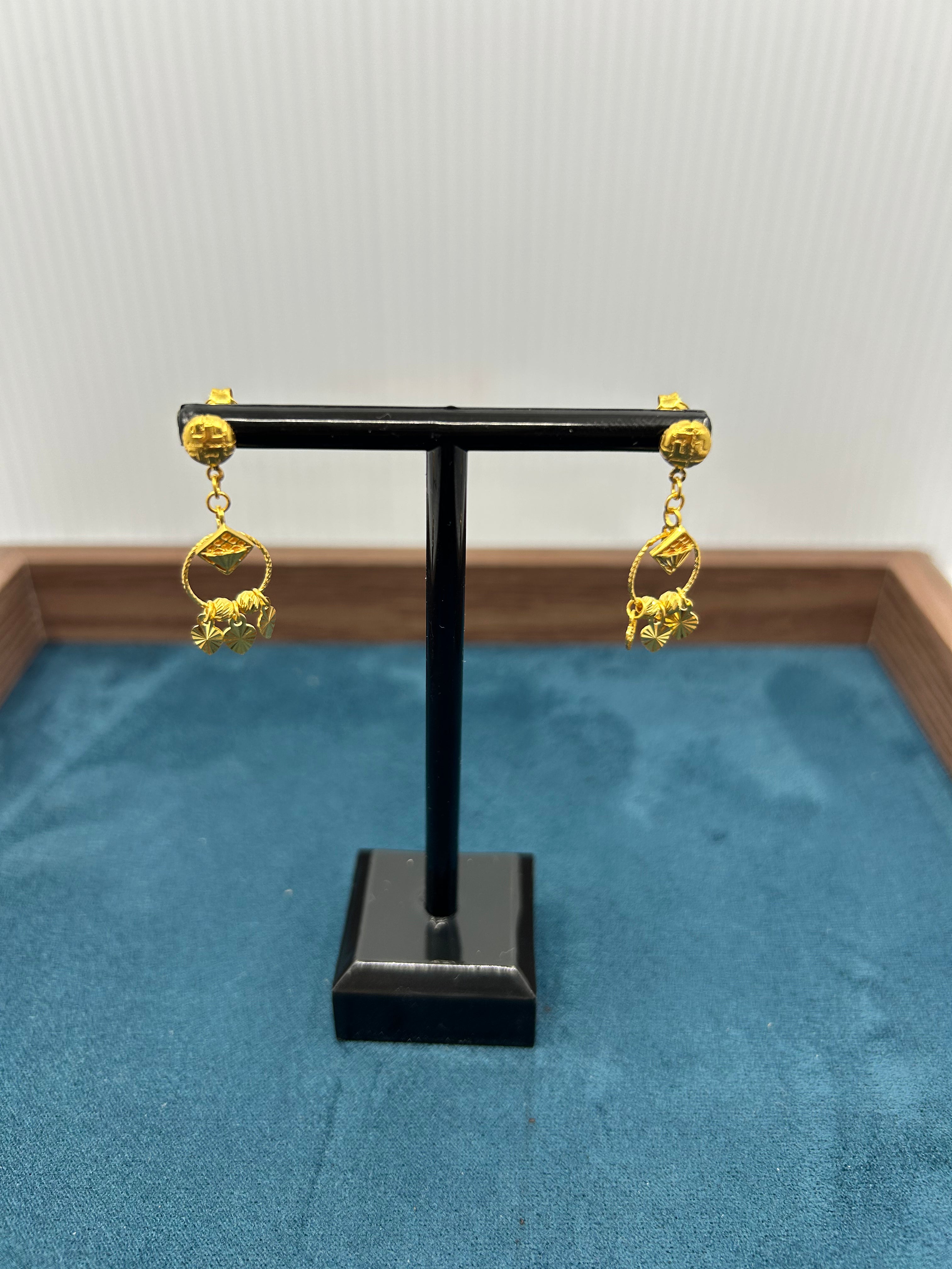 Gold earrings on a black stand against a blue fabric background