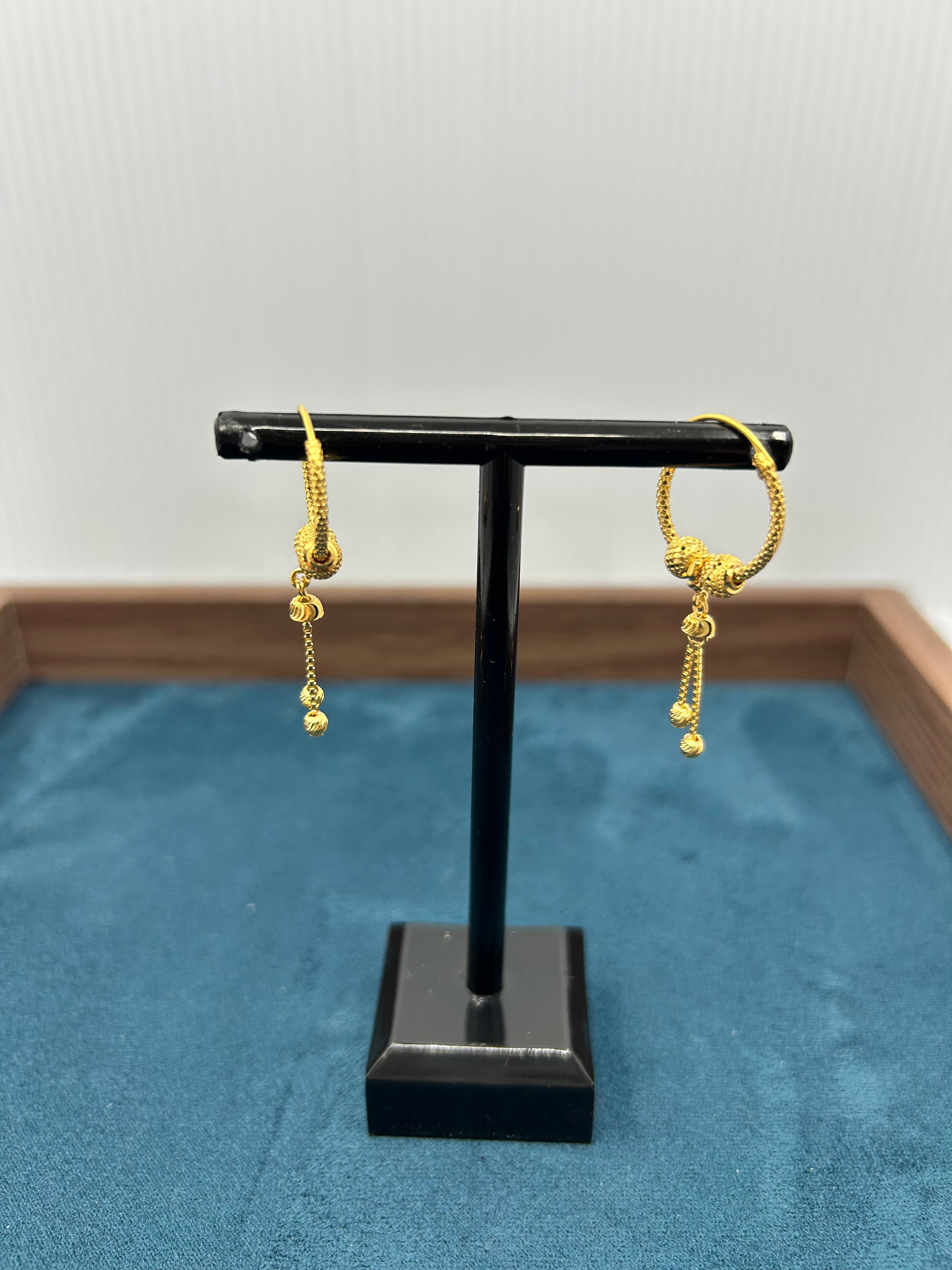 Gold earrings on a black display stand against a blue fabric background