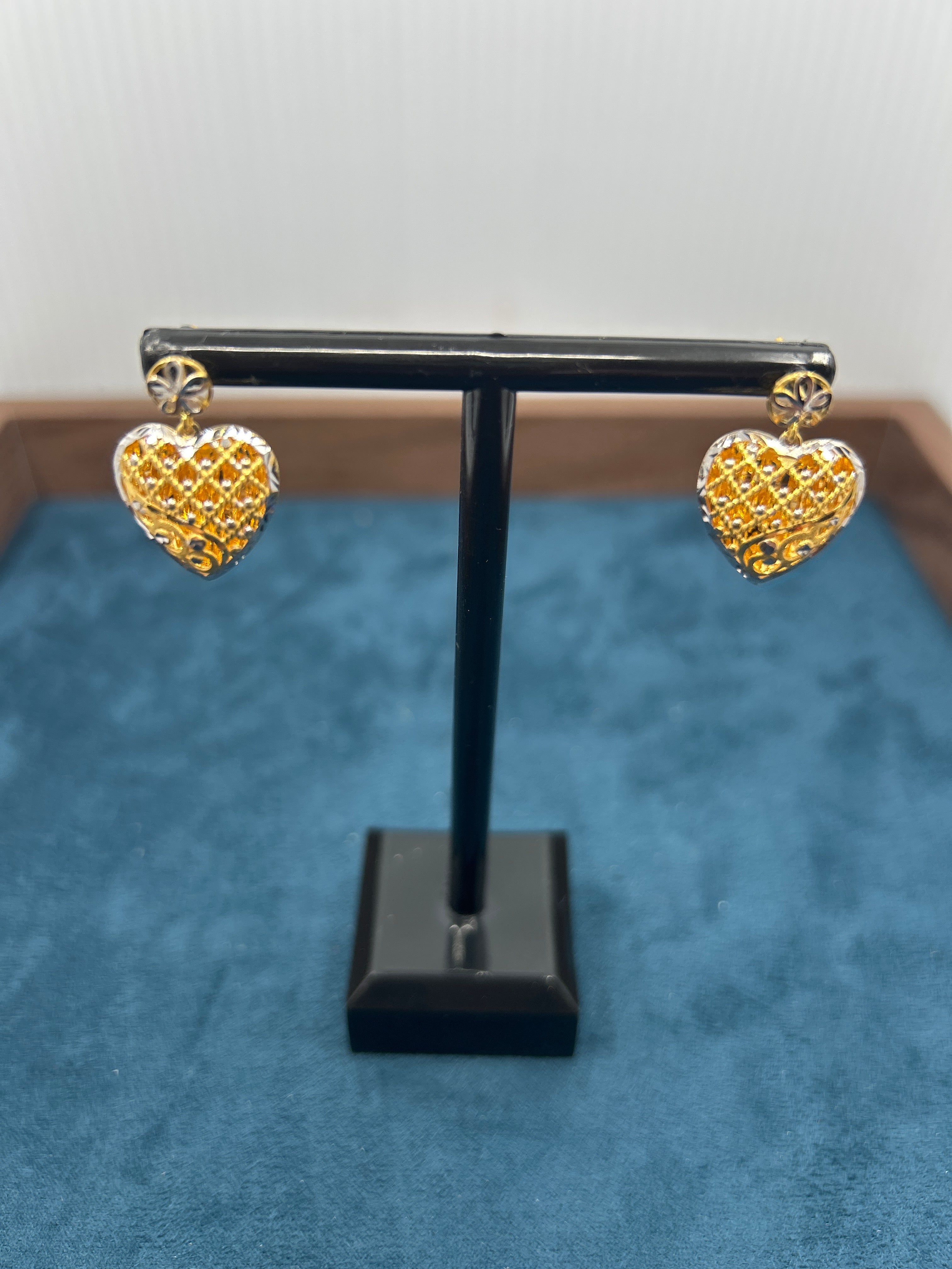Gold heart-shaped earrings on a black stand against a blue background