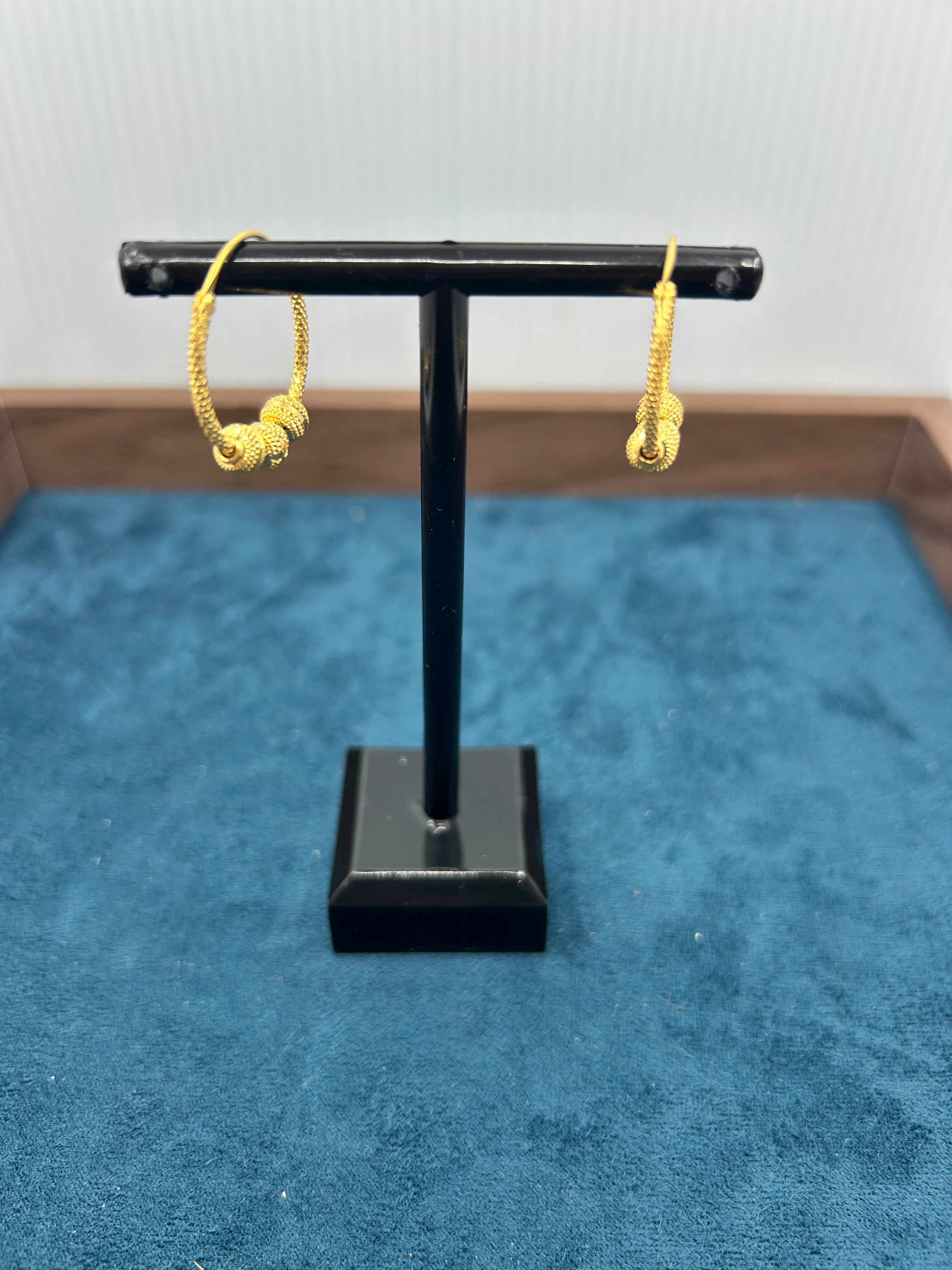 Gold hoop earrings on a black stand against a blue background
