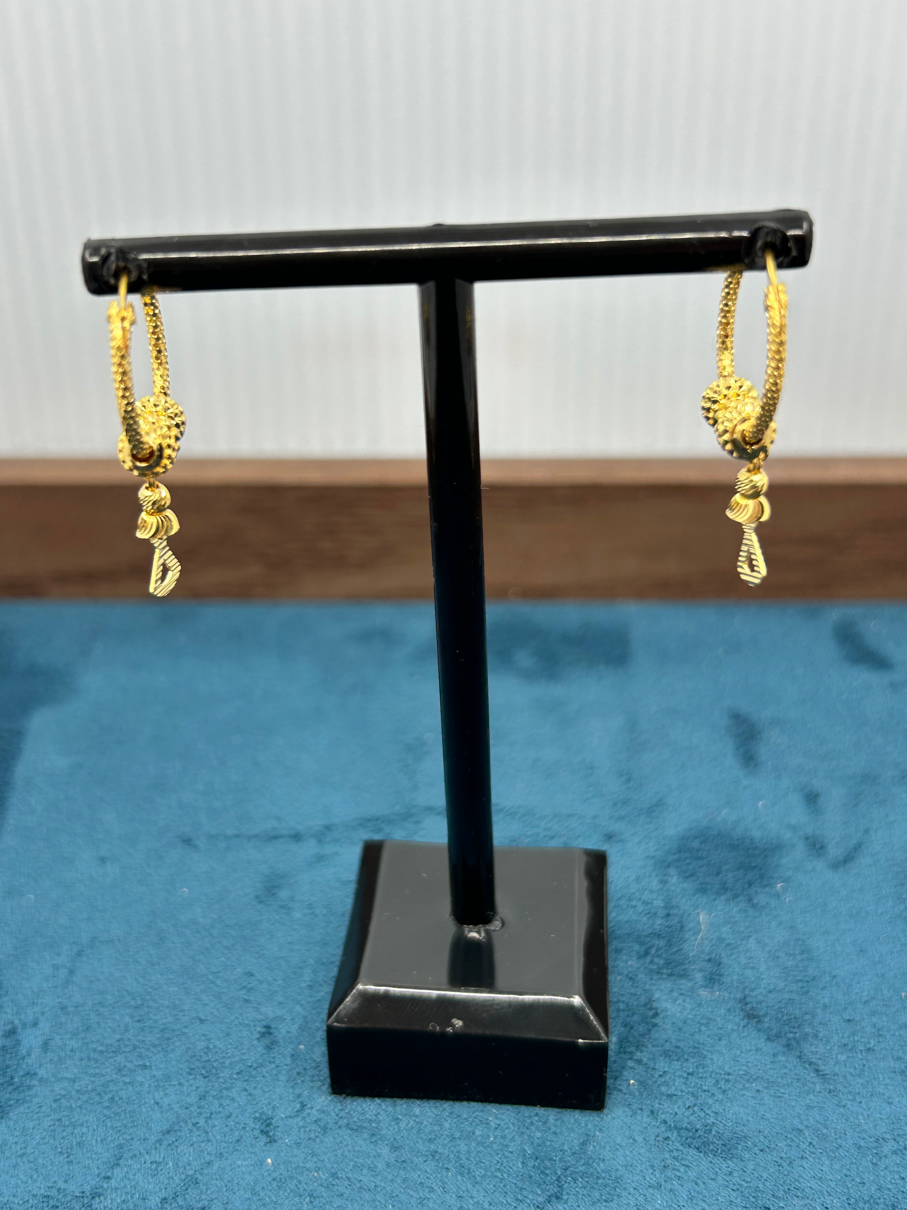Gold hoop earrings with small dangling charm on a black display stand