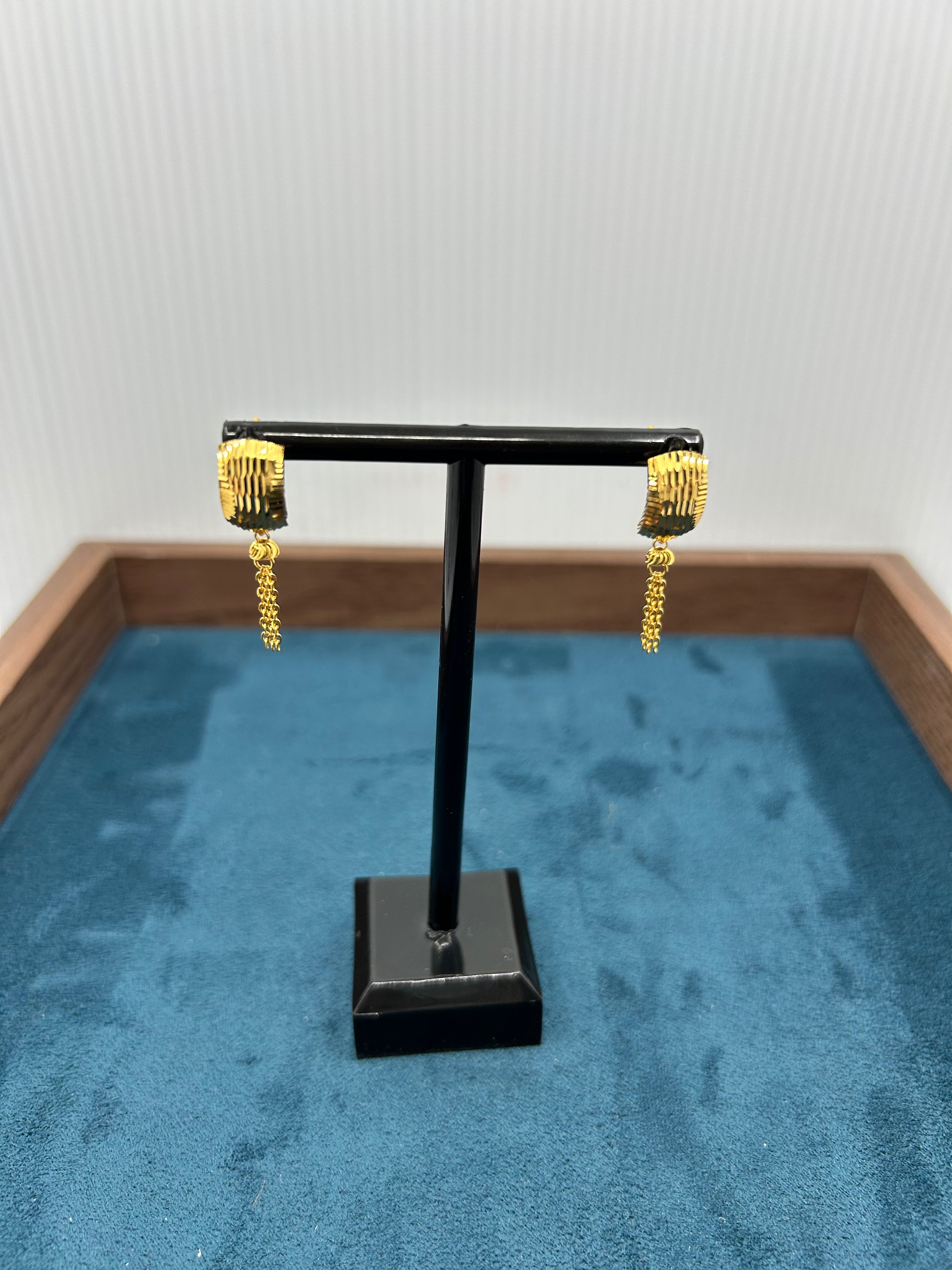 Gold hoop earrings on a black display stand against a white background