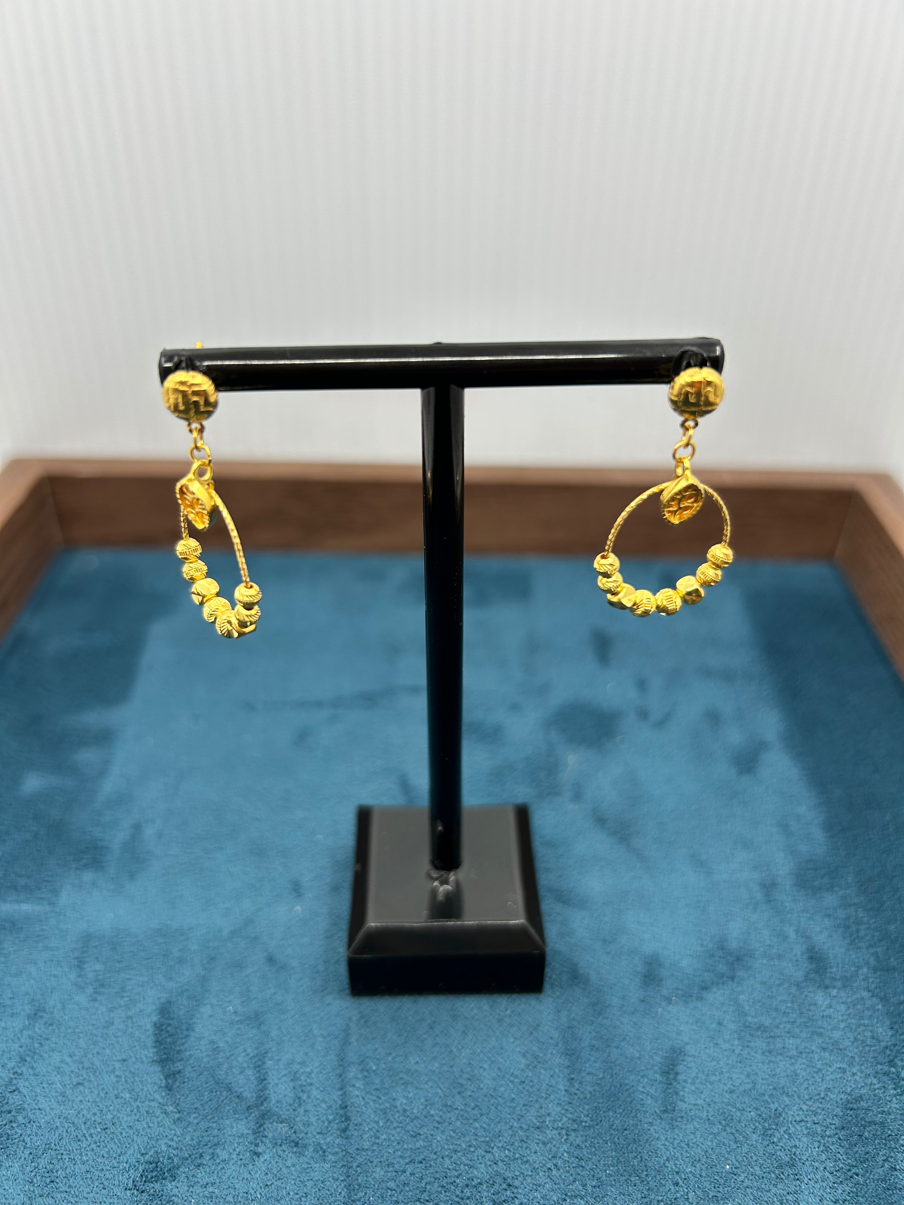 Gold hoop earrings on a black display stand against a blue fabric background