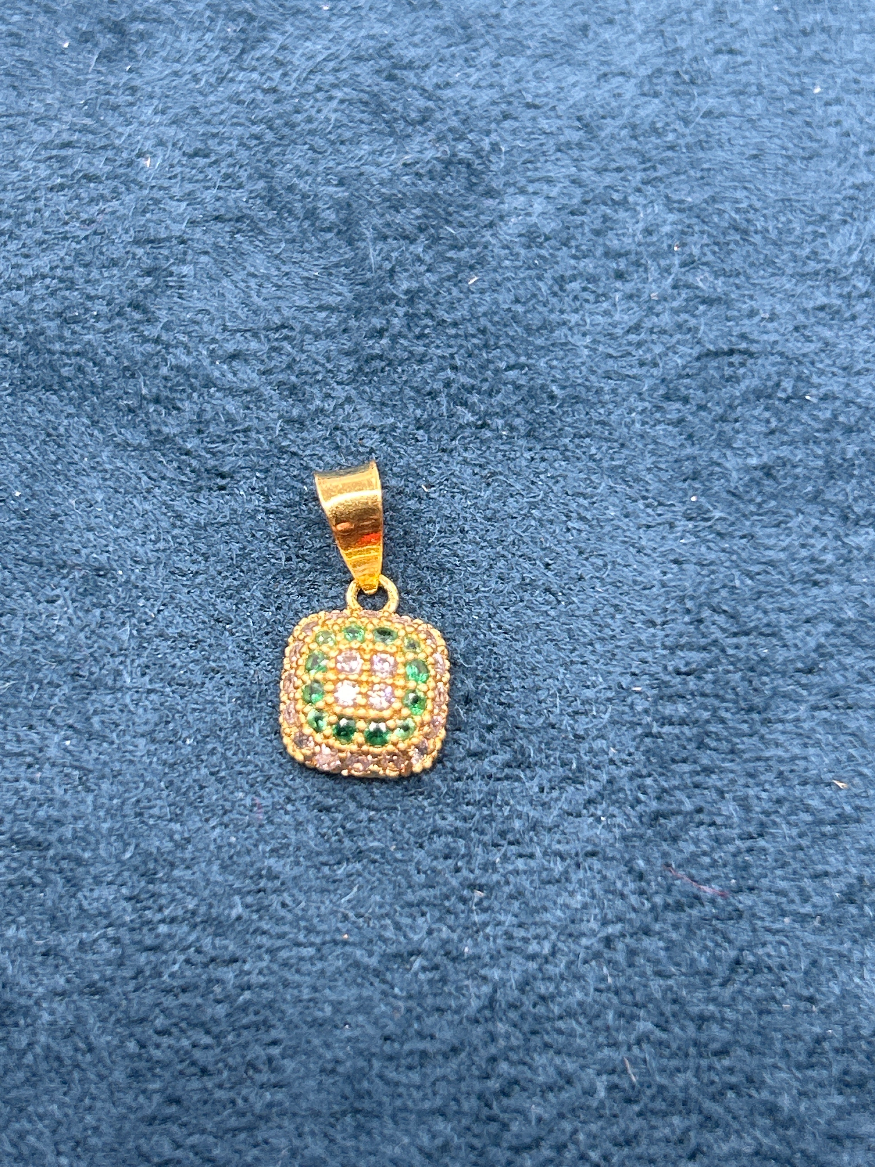 Gold pendant with green stones on a blue textured background