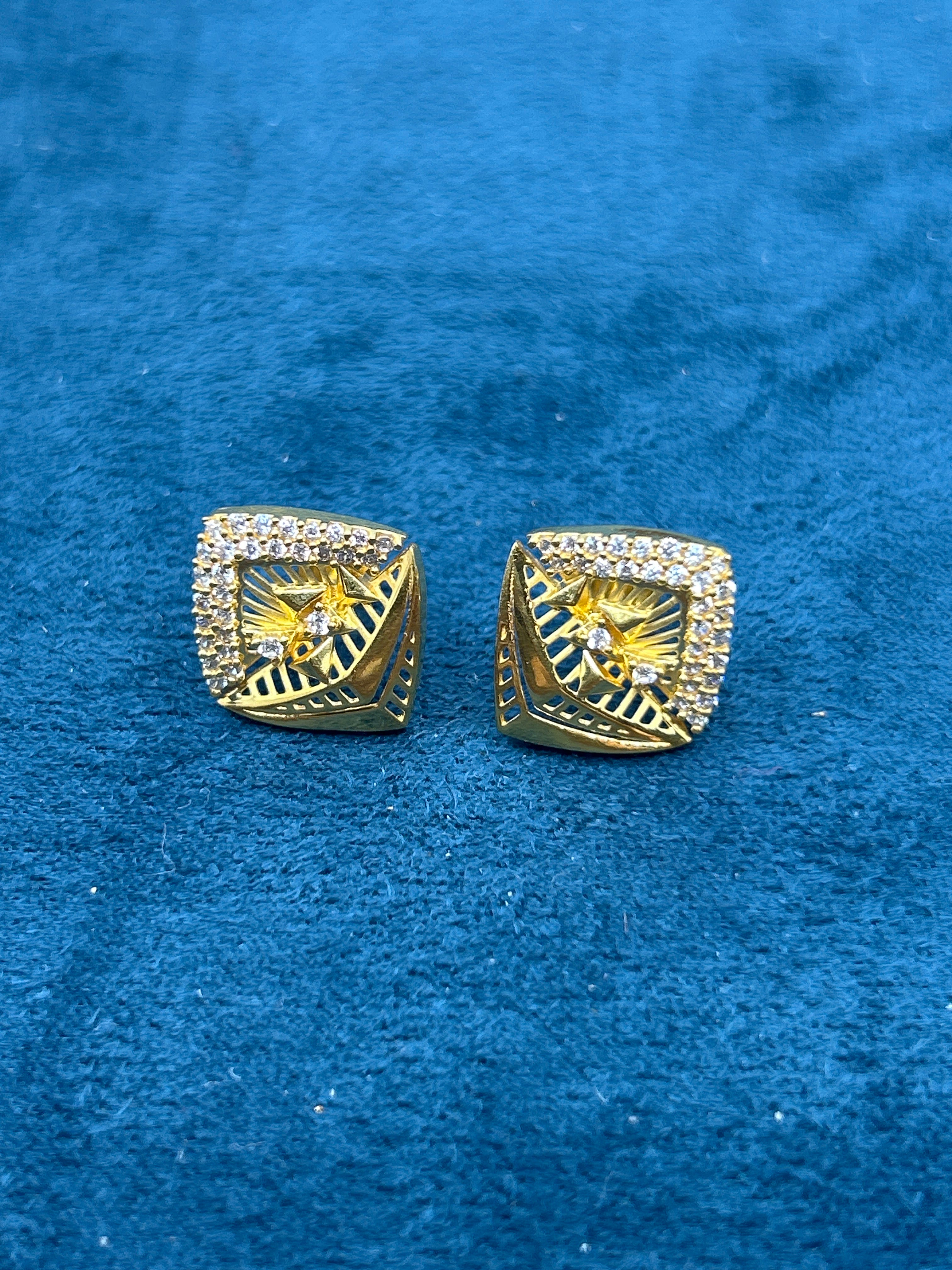 Gold square earrings with star design on a blue velvet background