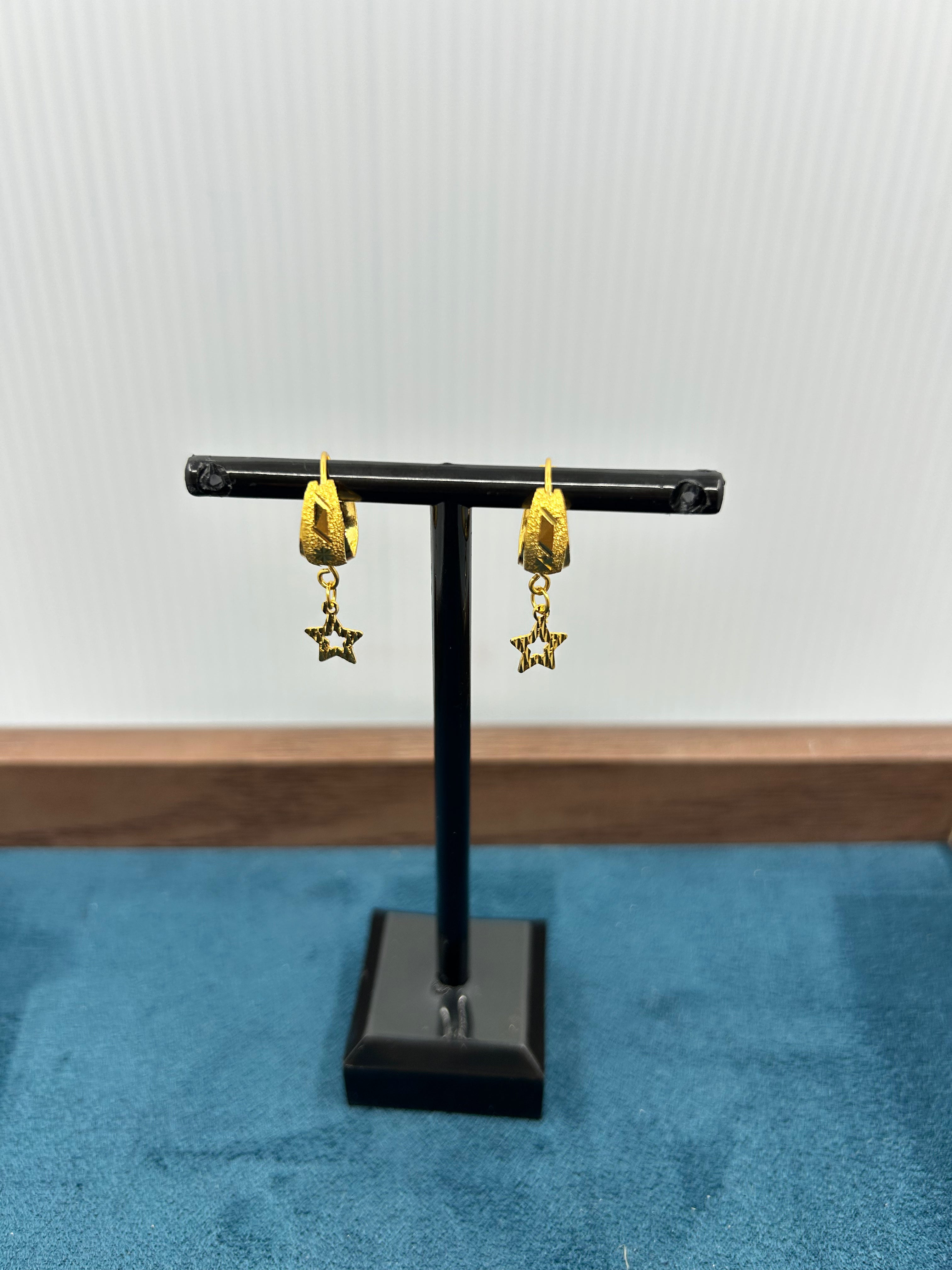 Gold star-shaped earrings on a black stand against a white background