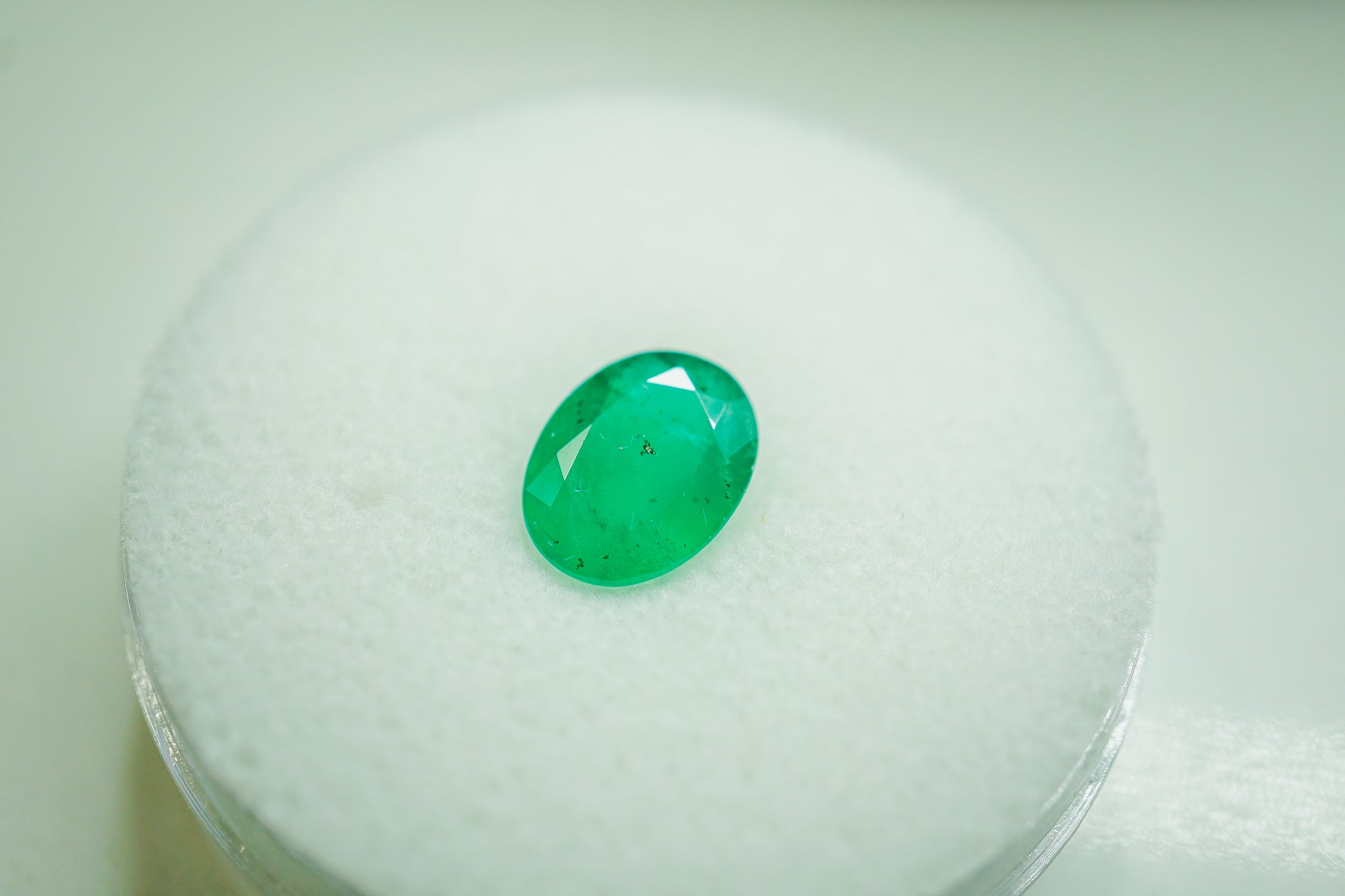 Green oval emerald gemstone placed on a white display pad (0.57 g
