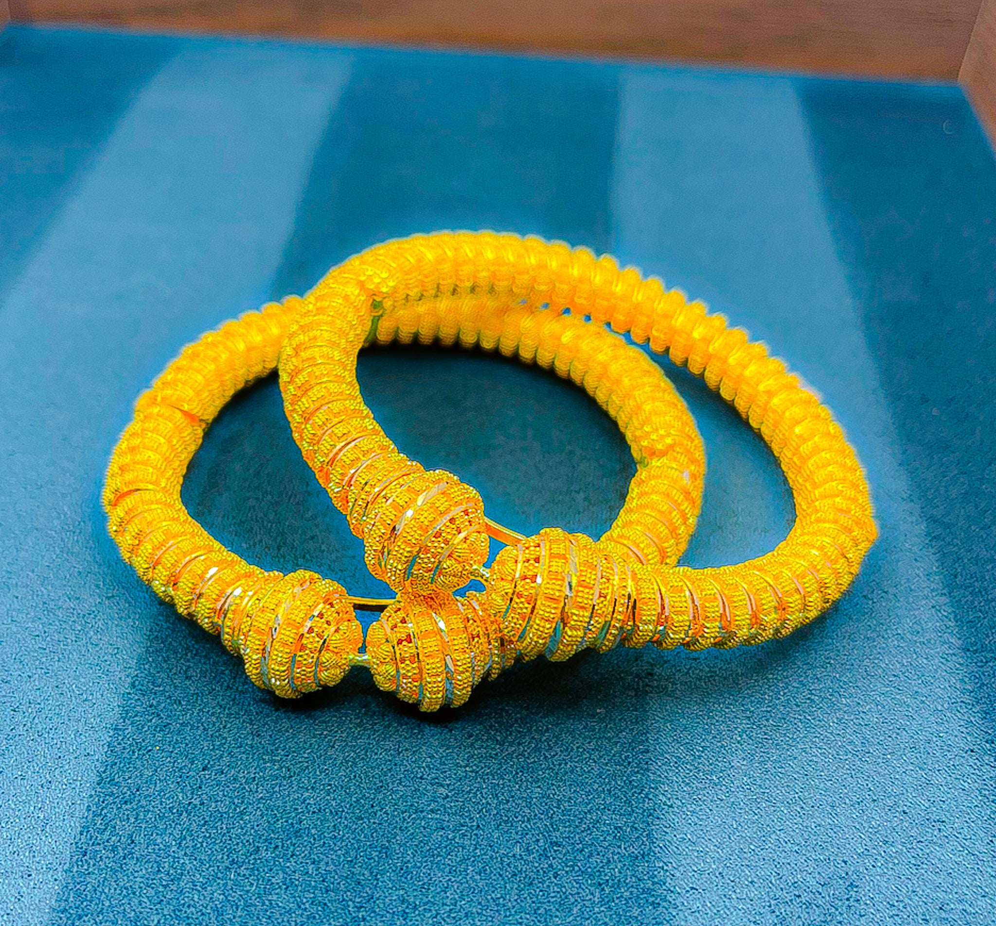 Handheld close-up of 22K gold bangle set (2 PCS) with ribbed coil texture and decorative end caps