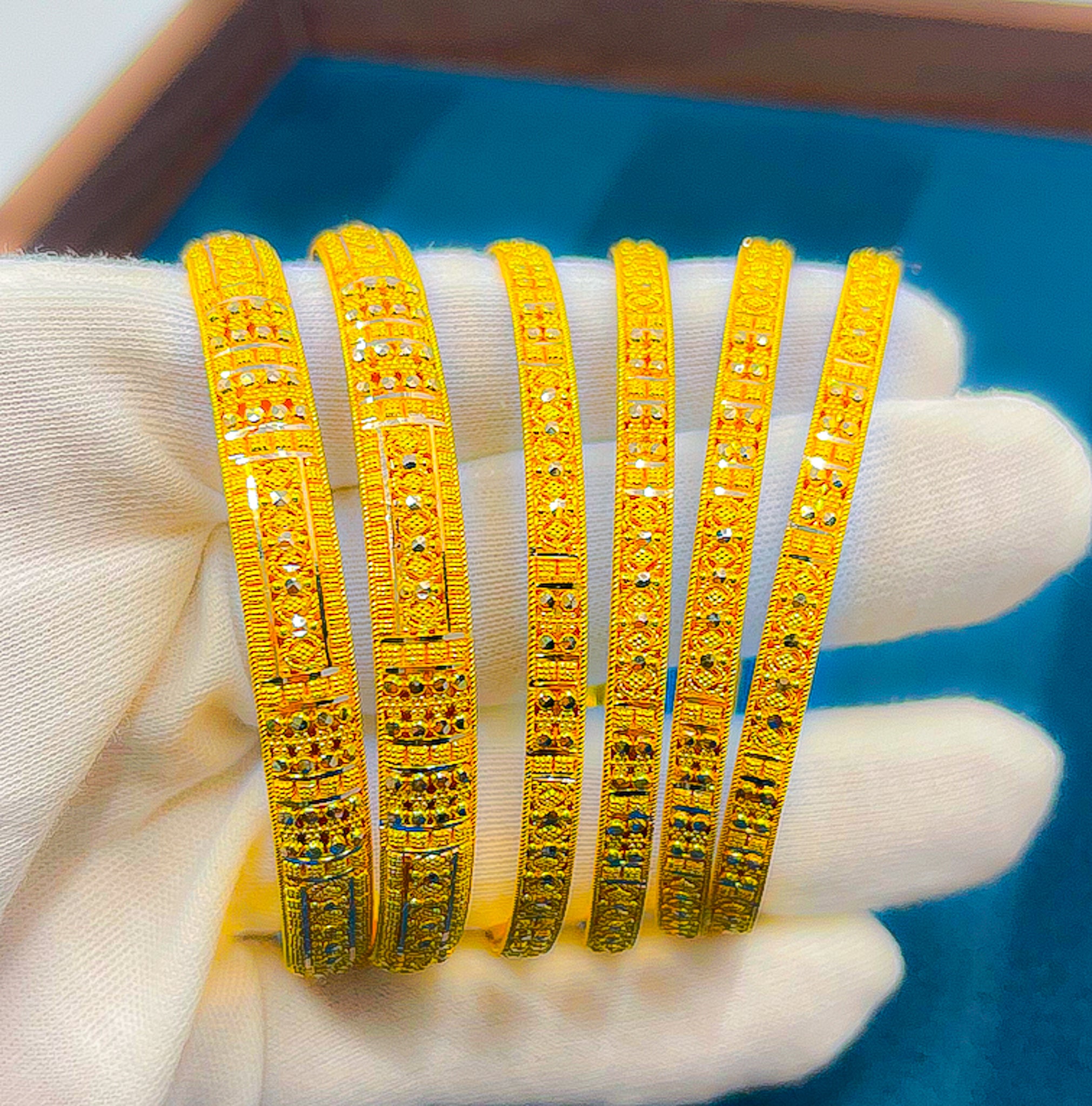 Handheld close-up of 6 slim 22K yellow gold bangles showing engraved patterned detailing