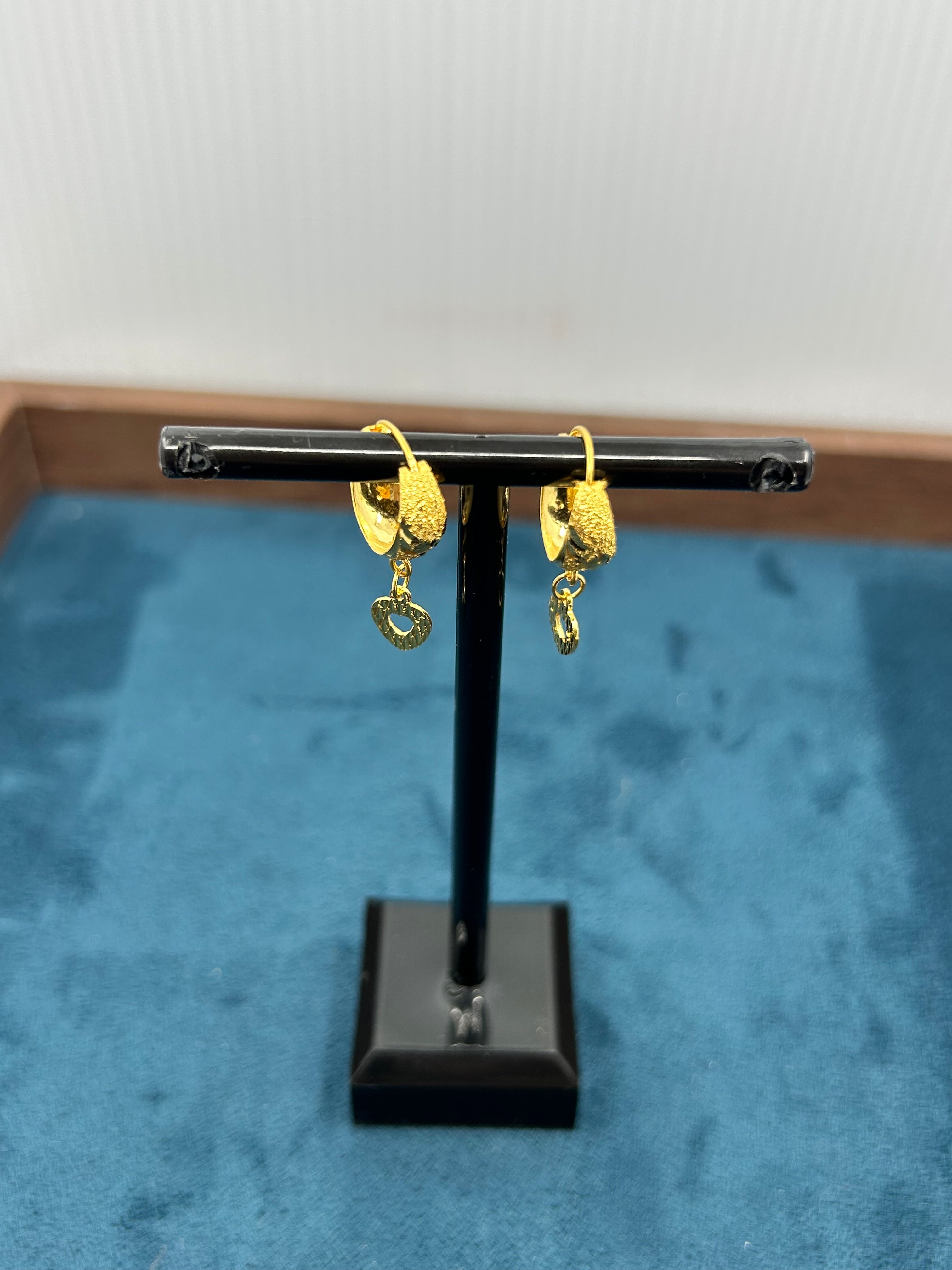 Gold earrings on a black stand against a blue background