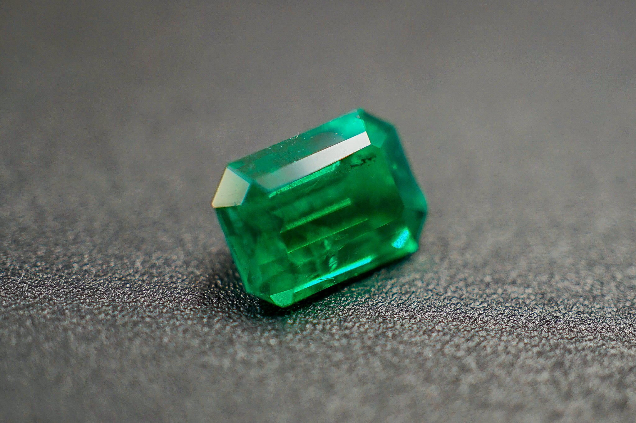 Loose emerald gemstone 0.17 g with rectangular emerald cut on gray textured background