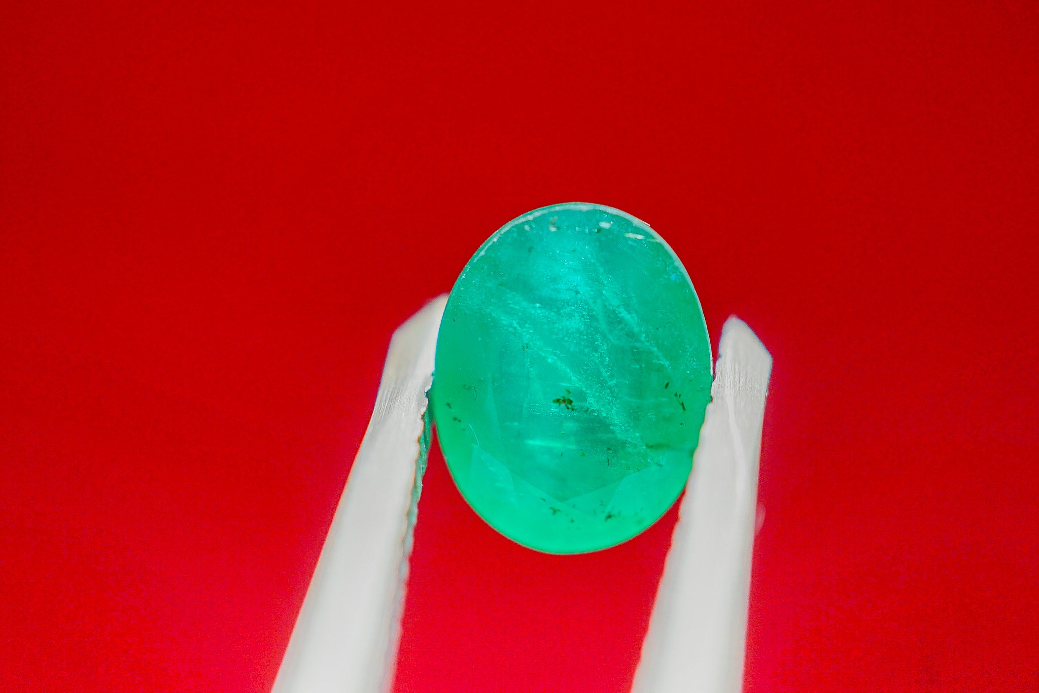 Loose green emerald gemstone held in tweezers against a red background (0.57 g