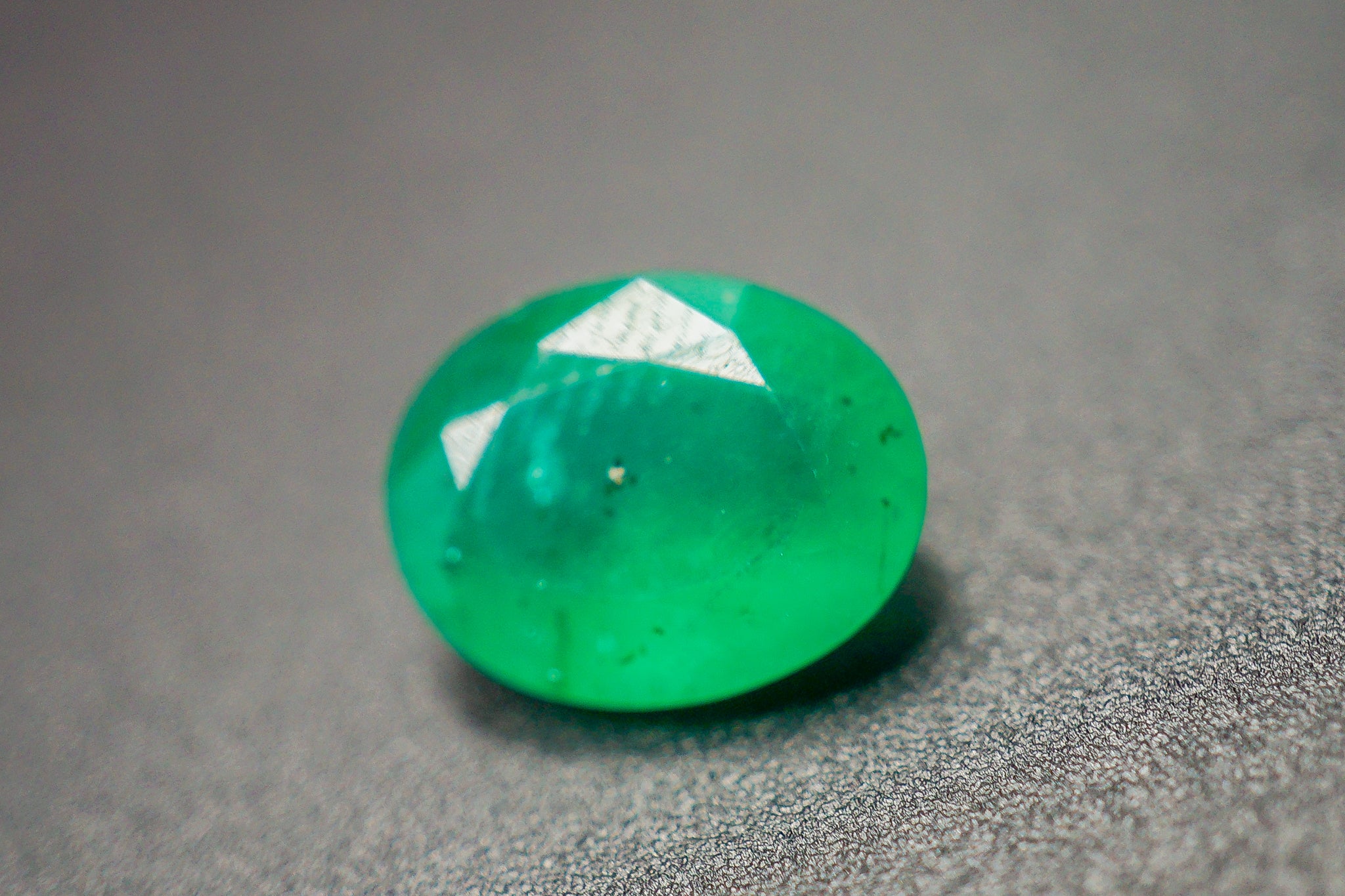 Loose green emerald stone in an oval shape on a gray background