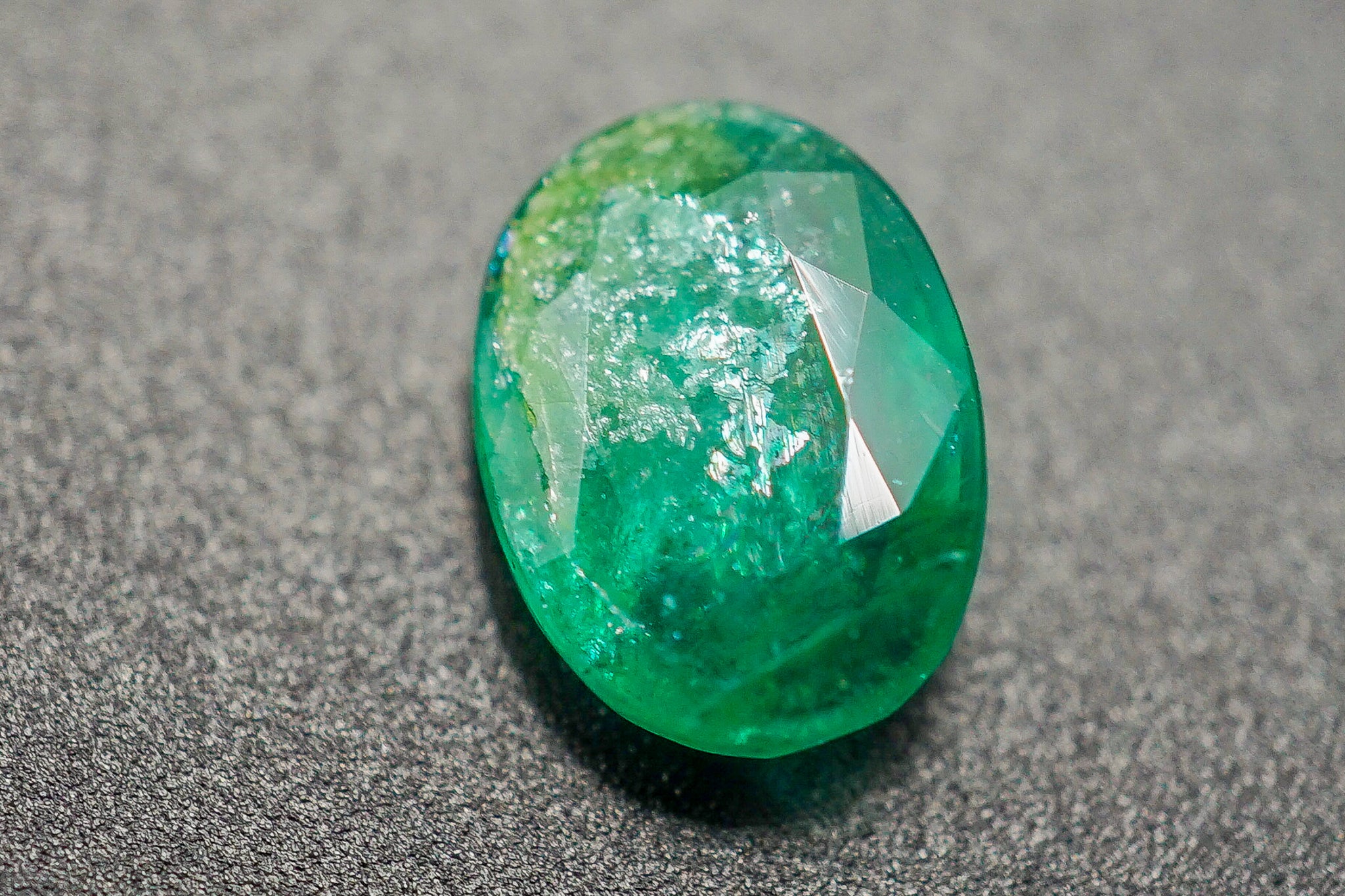 Oval green emerald gemstone held in tweezers on a red background