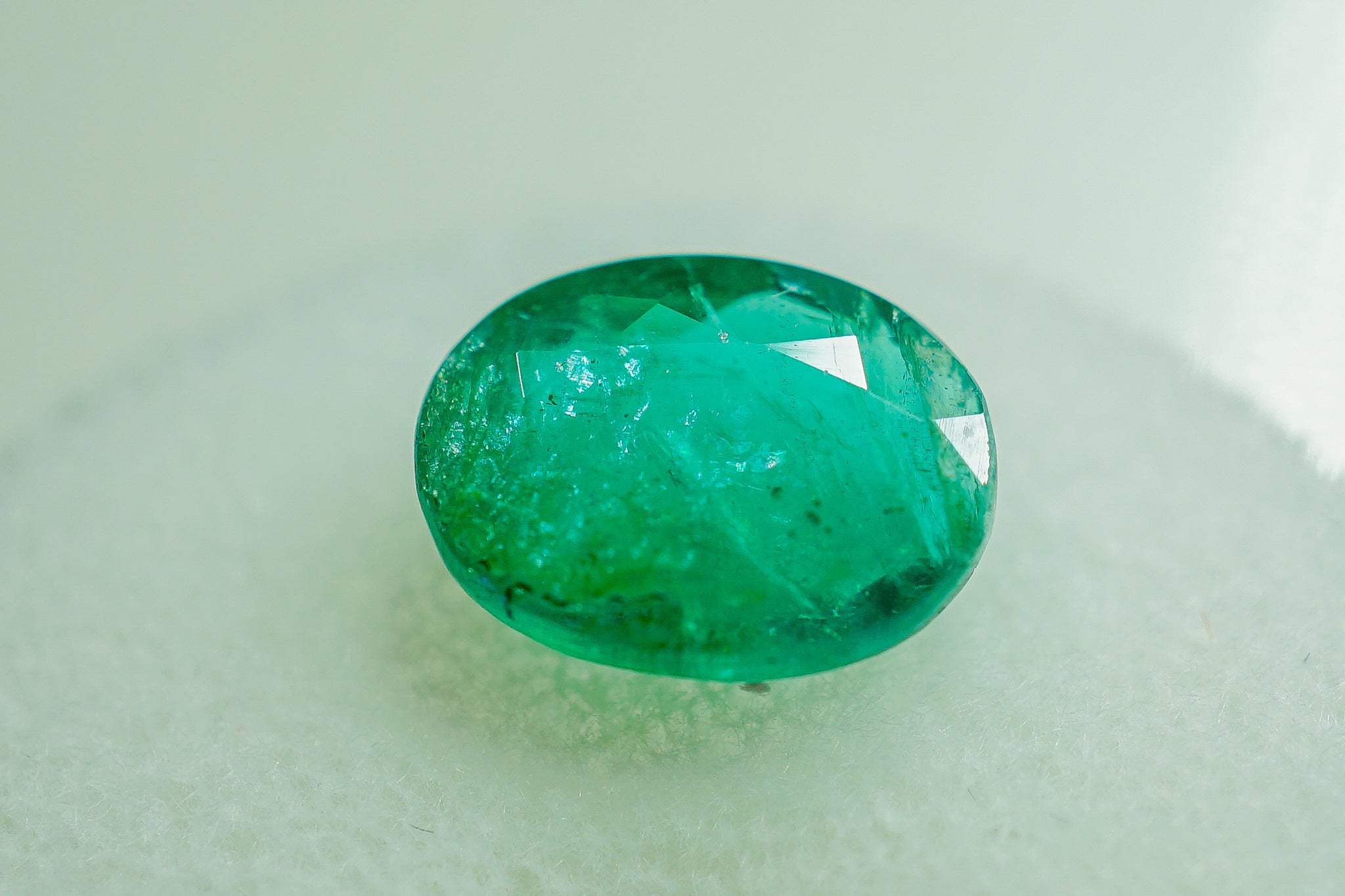 Oval green emerald gemstone photographed on a light background