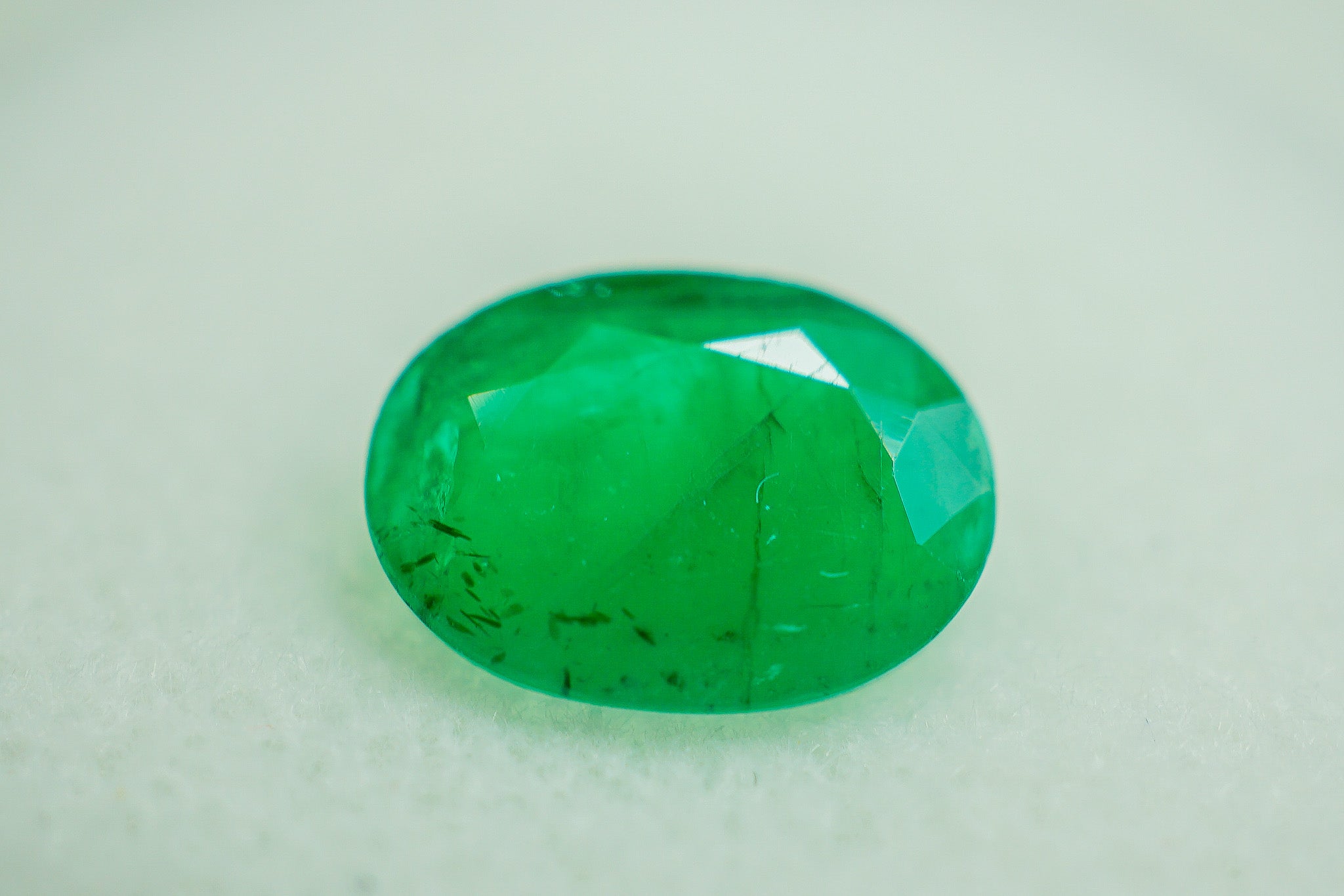 Oval green emerald gemstone photographed on a light background