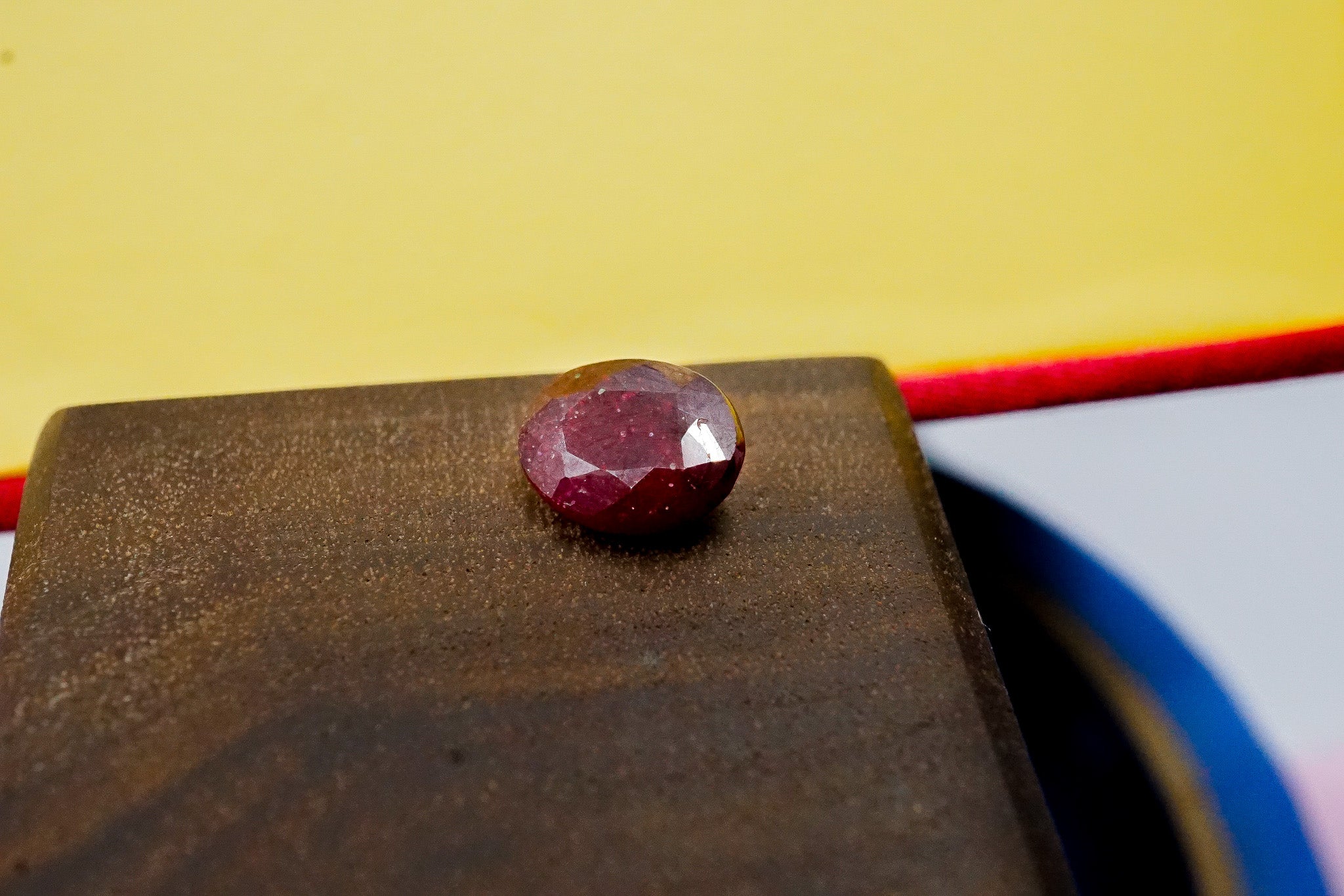 Oval ruby gemstone held with tweezers showing faceted cut and red tone