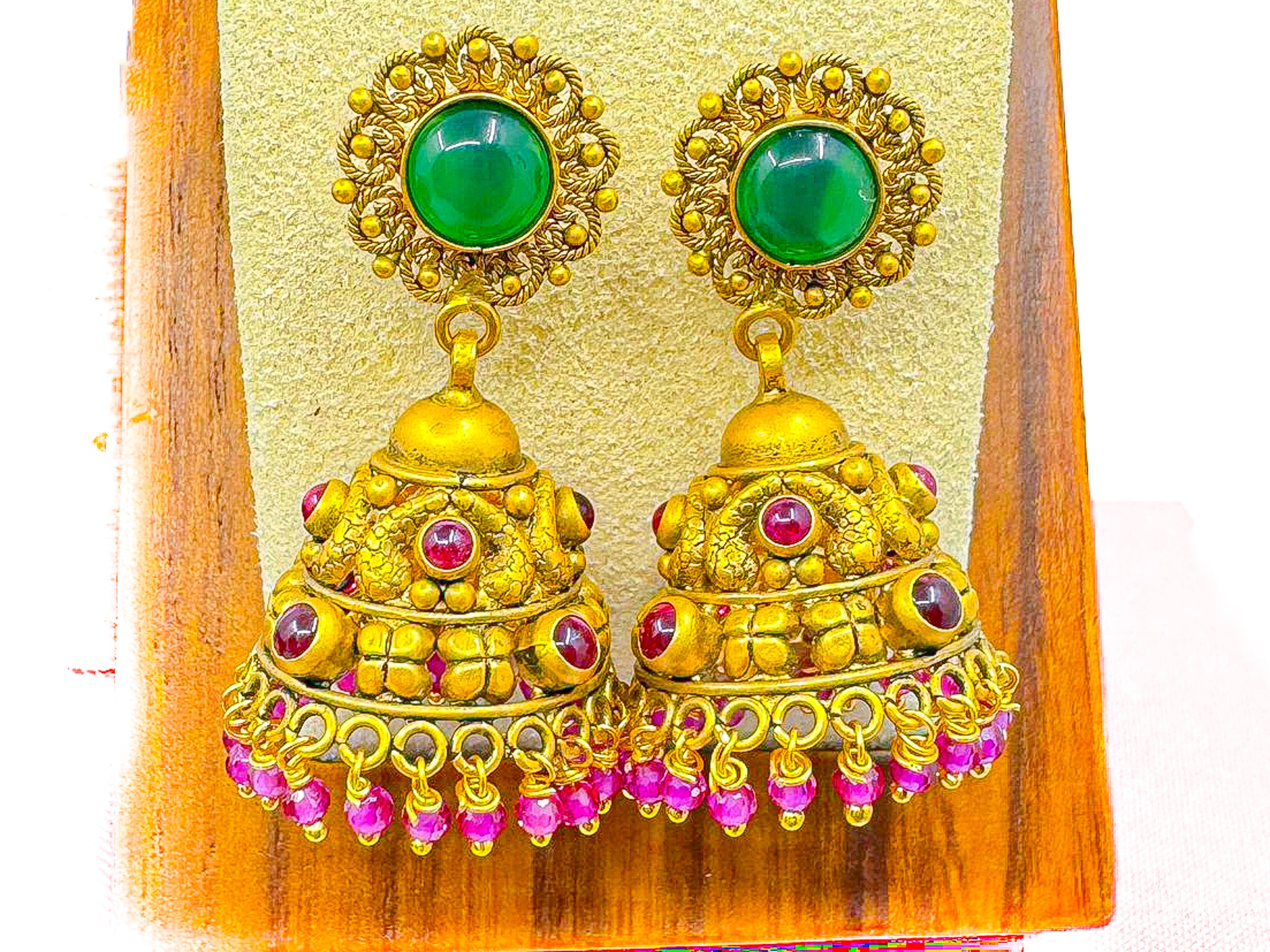 Pair of 22K gold jhumka earrings 13.82g with green top stones and pink accents on a yellow display card