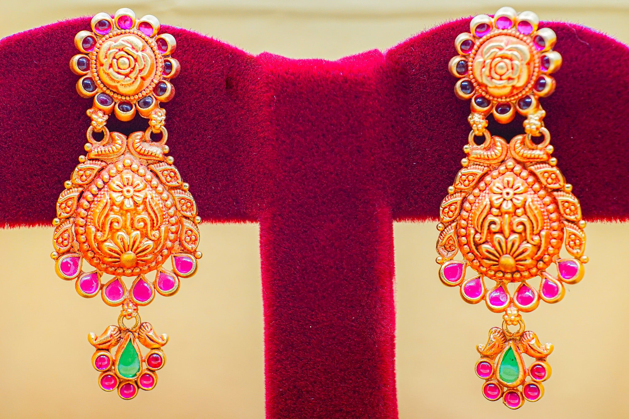 Pair of 22K gold jhumka earrings 9.84g with pink stones and green teardrop accents on a velvet stand