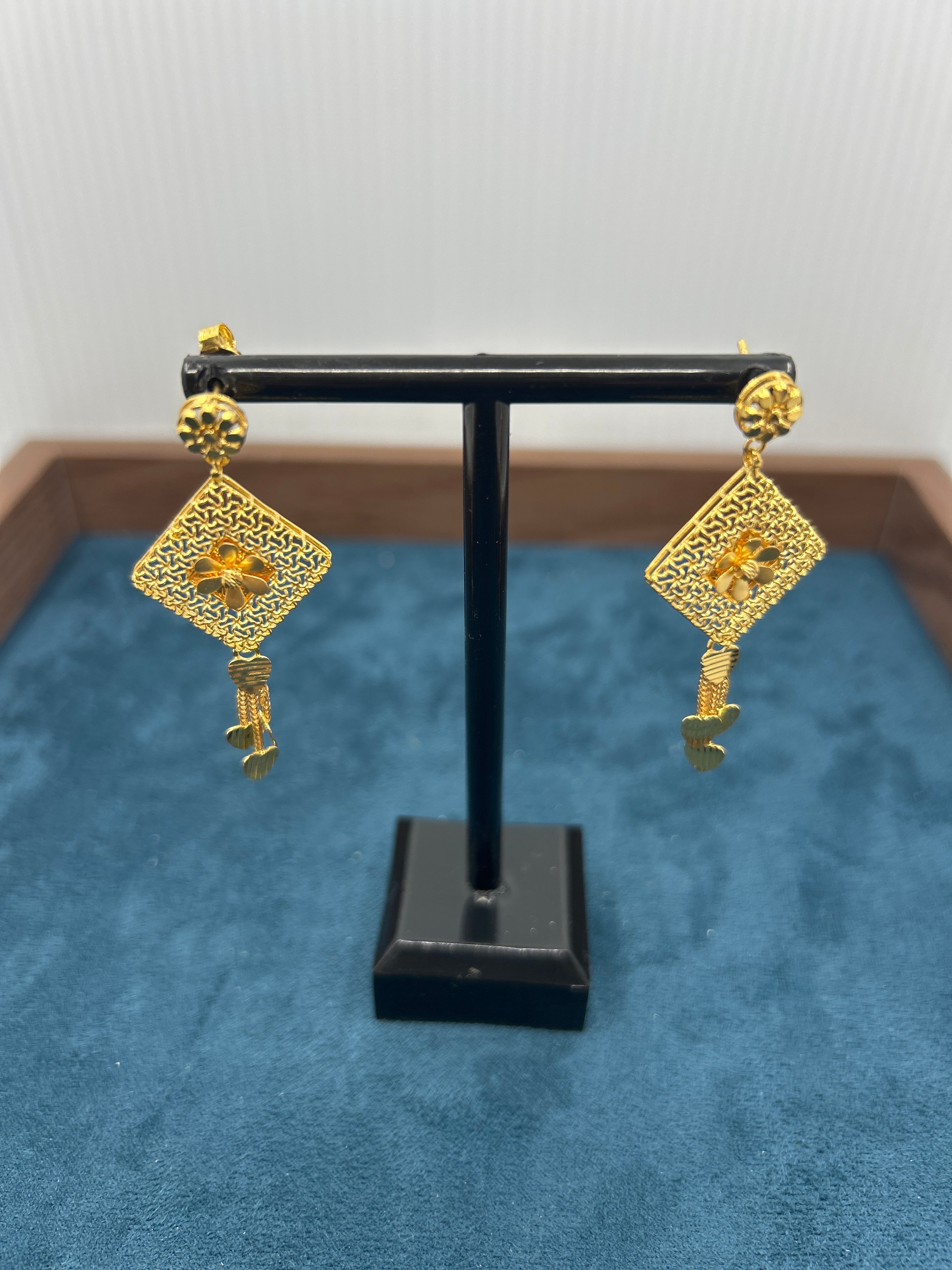 Pair of gold earrings on a black stand against a blue background