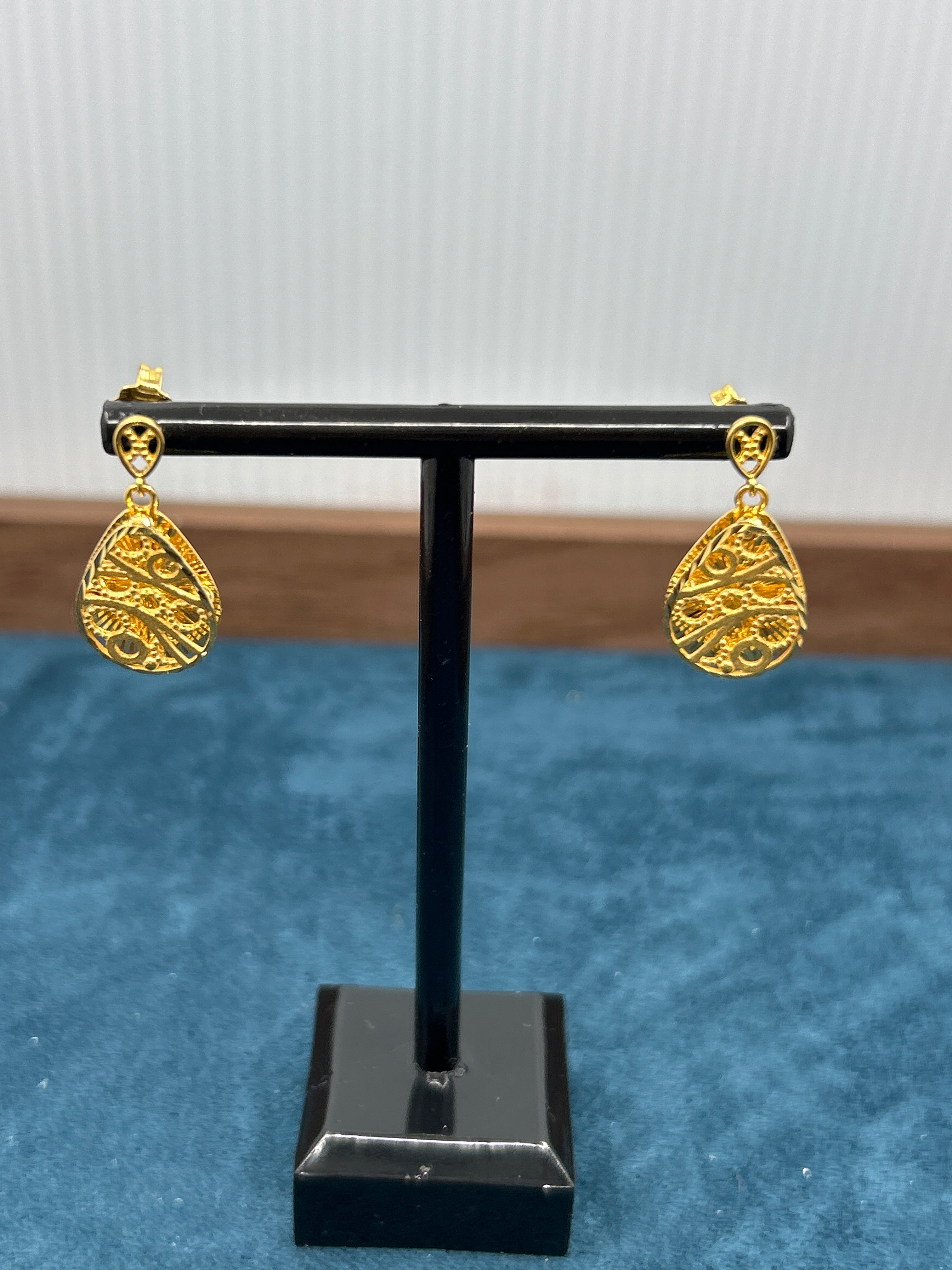 Pair of gold earrings on a black stand against a blue background