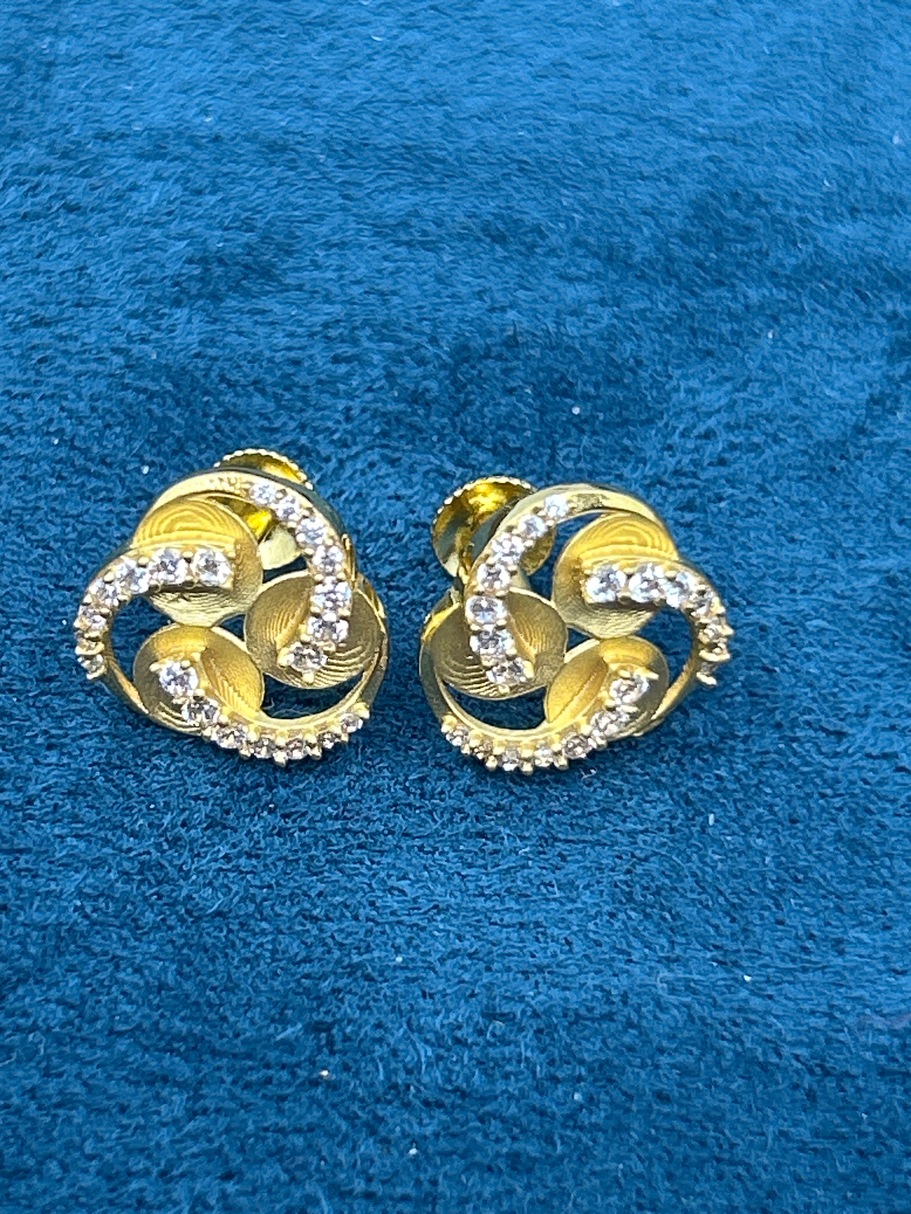 Pair of gold earrings with diamond-like stones on a blue textured background