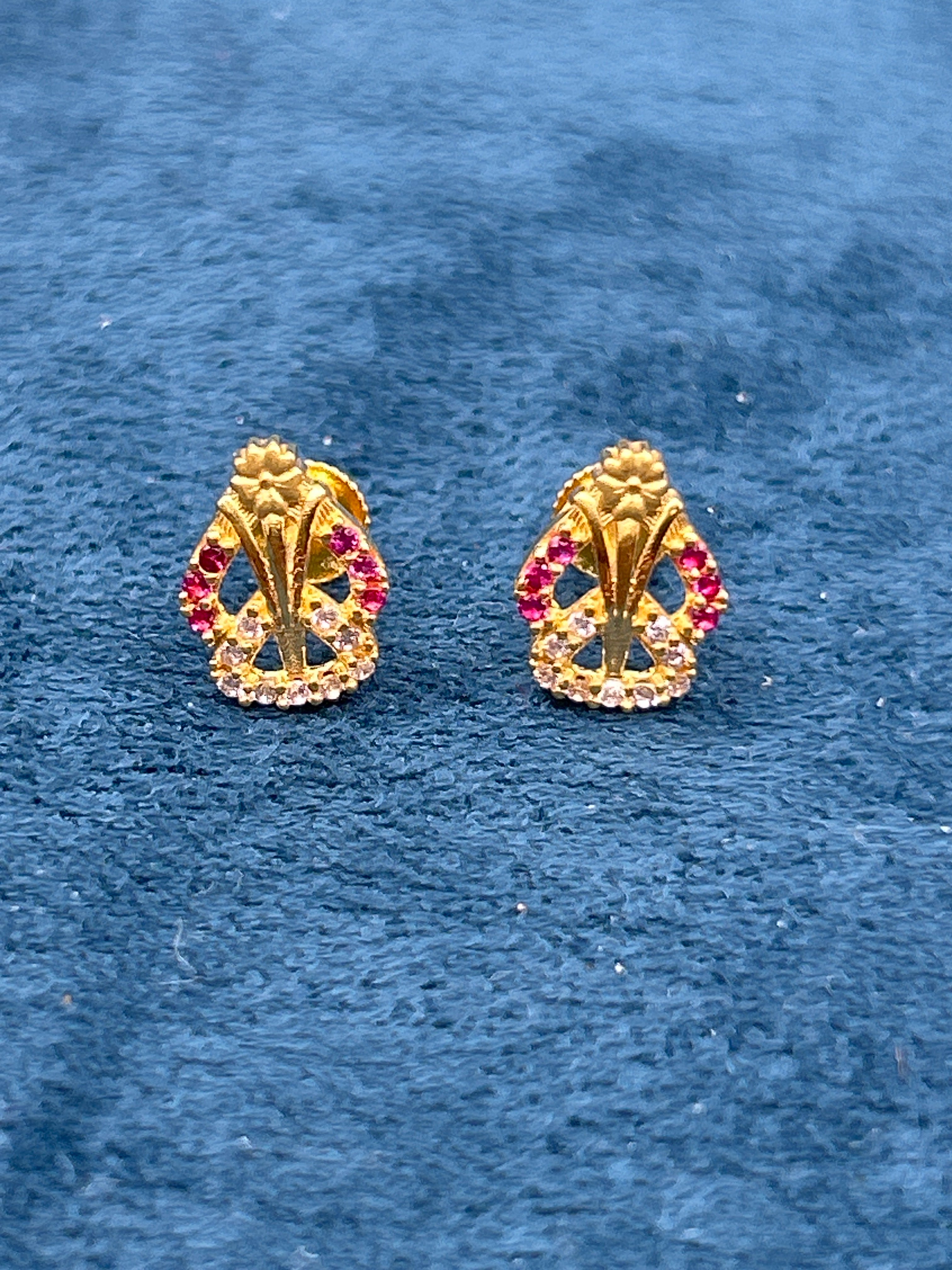 Pair of gold earrings with red gemstones on a blue textured background