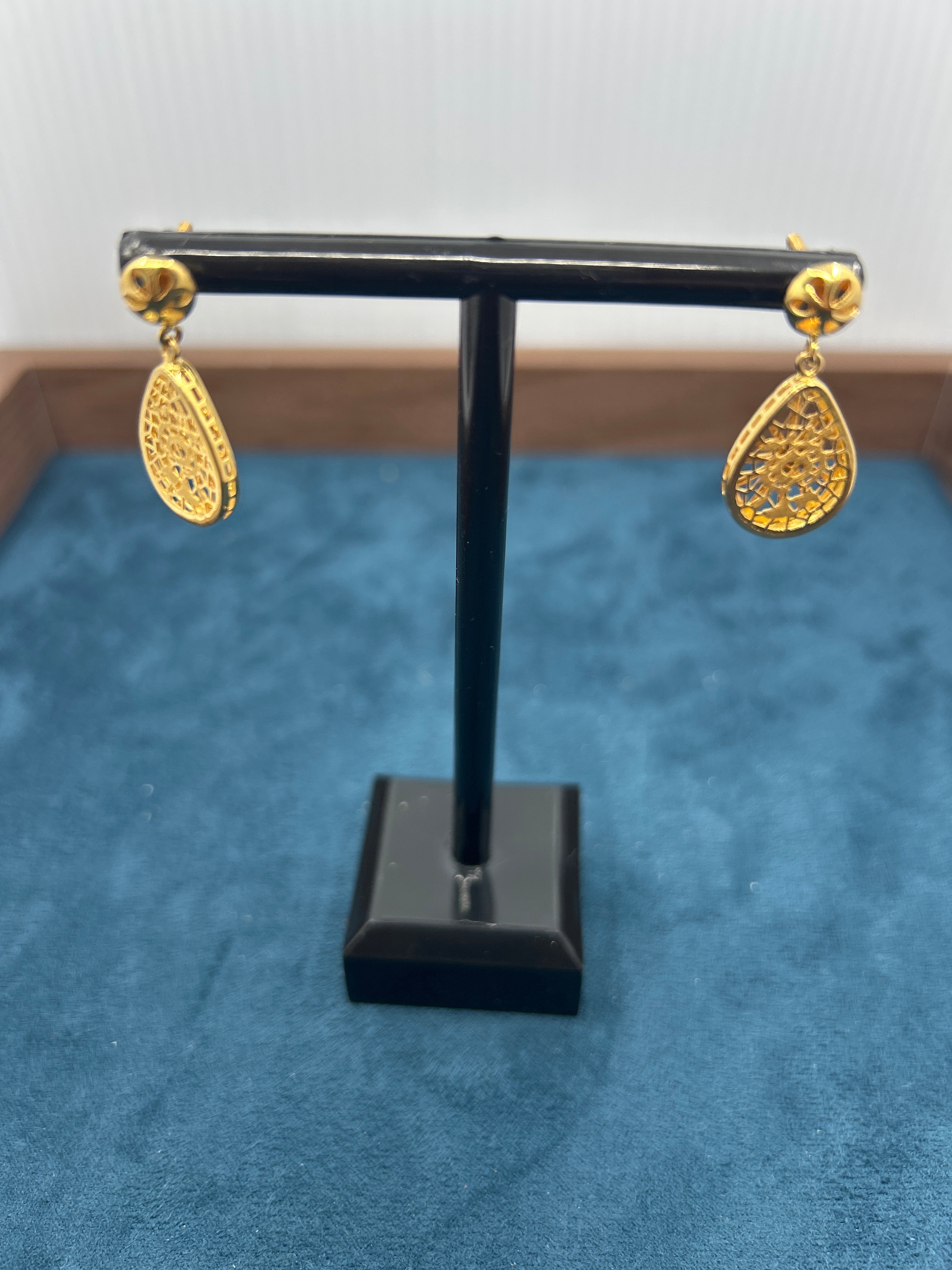 Pair of gold earrings on a black stand against a blue background