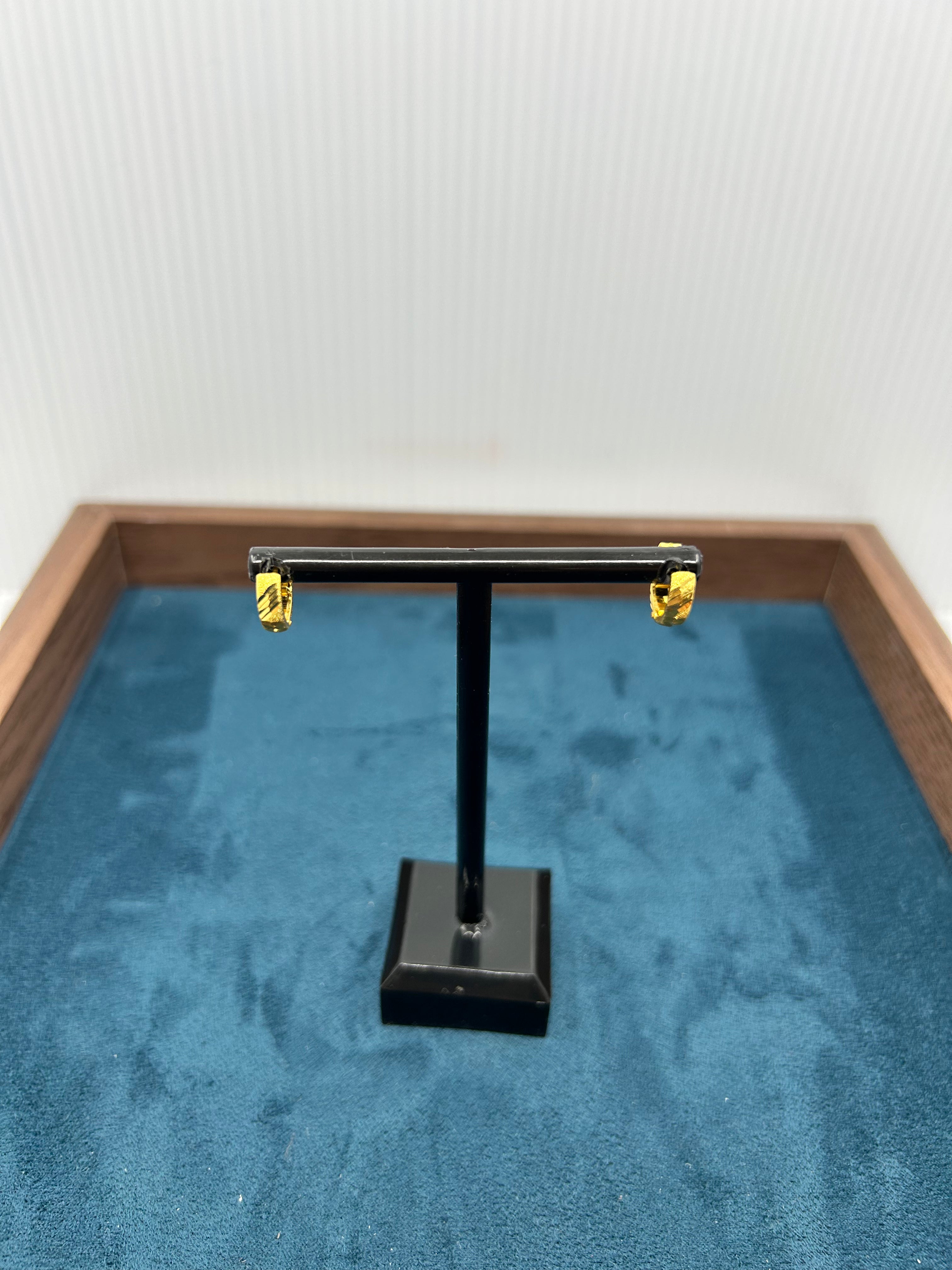 Pair of textured gold huggie earrings on a black T-stand over a blue fabric background