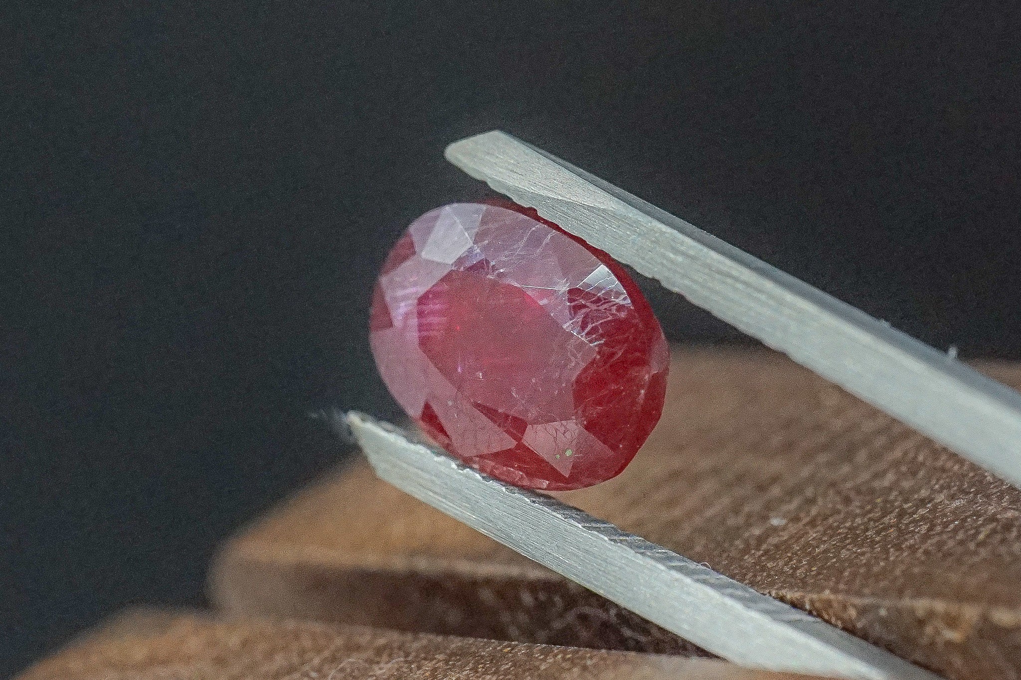 Round red ruby gemstone held in tweezers on a dark background