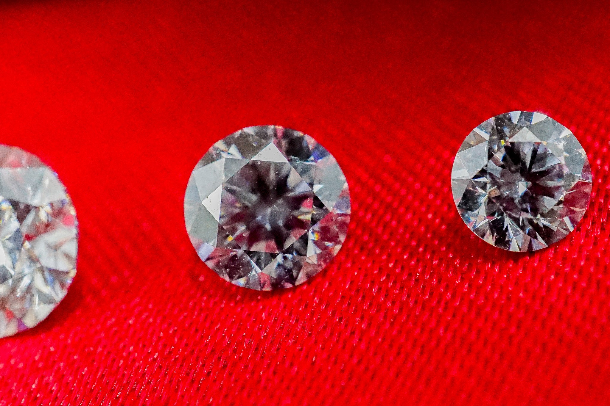 Set of four loose diamonds arranged in a row on red fabric.