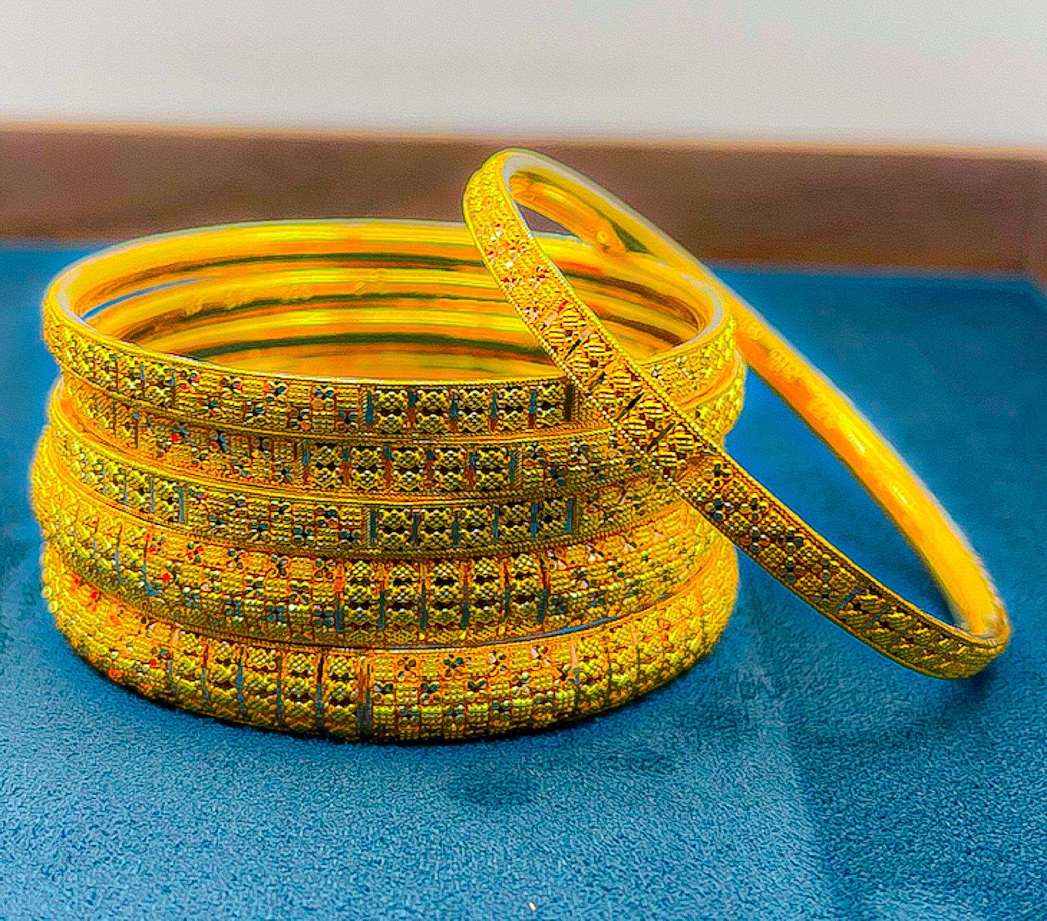 Six 22k yellow gold bangles with engraved pattern on a blue velvet tray