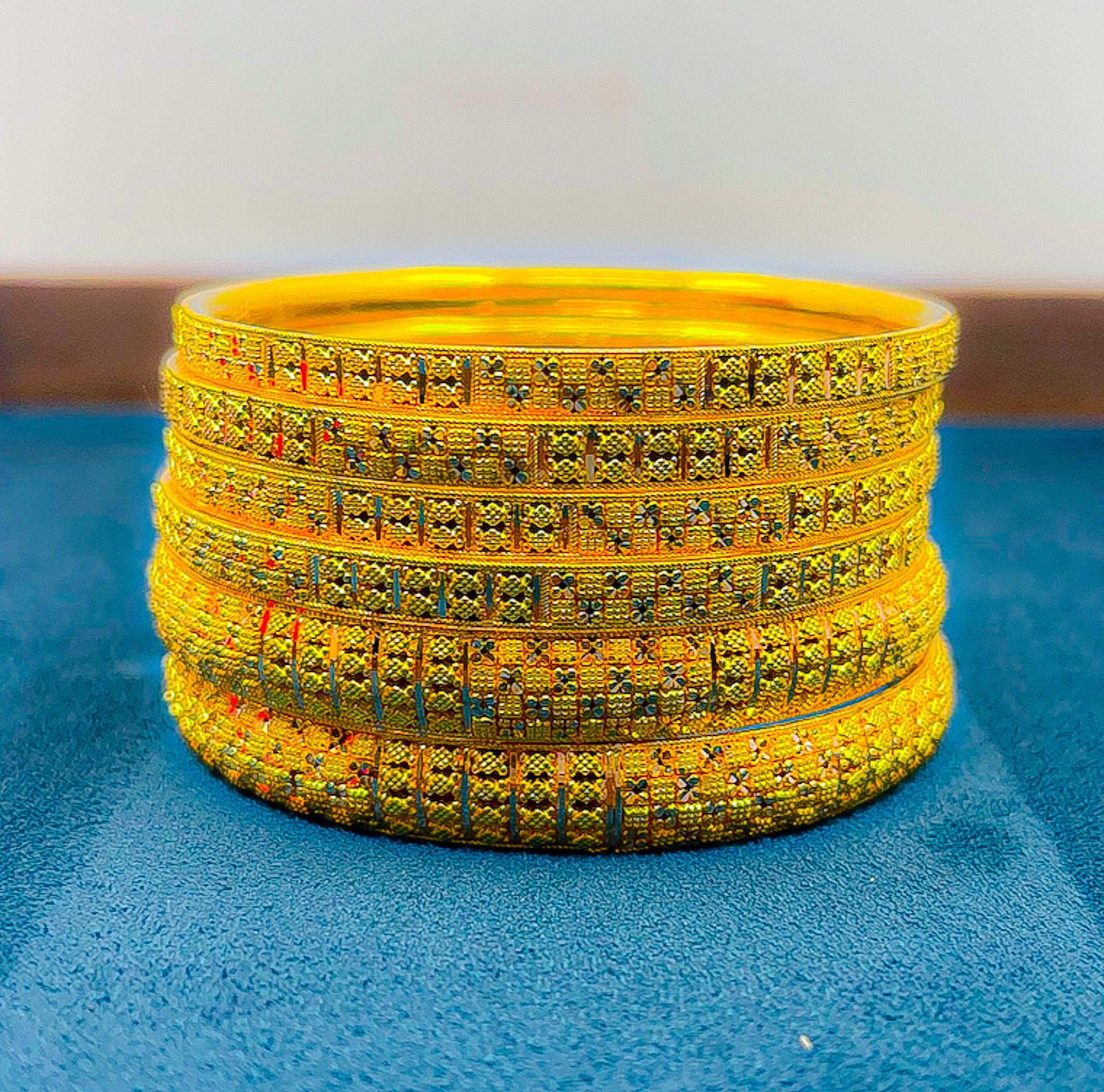 Stacked slim 22k gold bangles with intricate engraved texture on blue tray