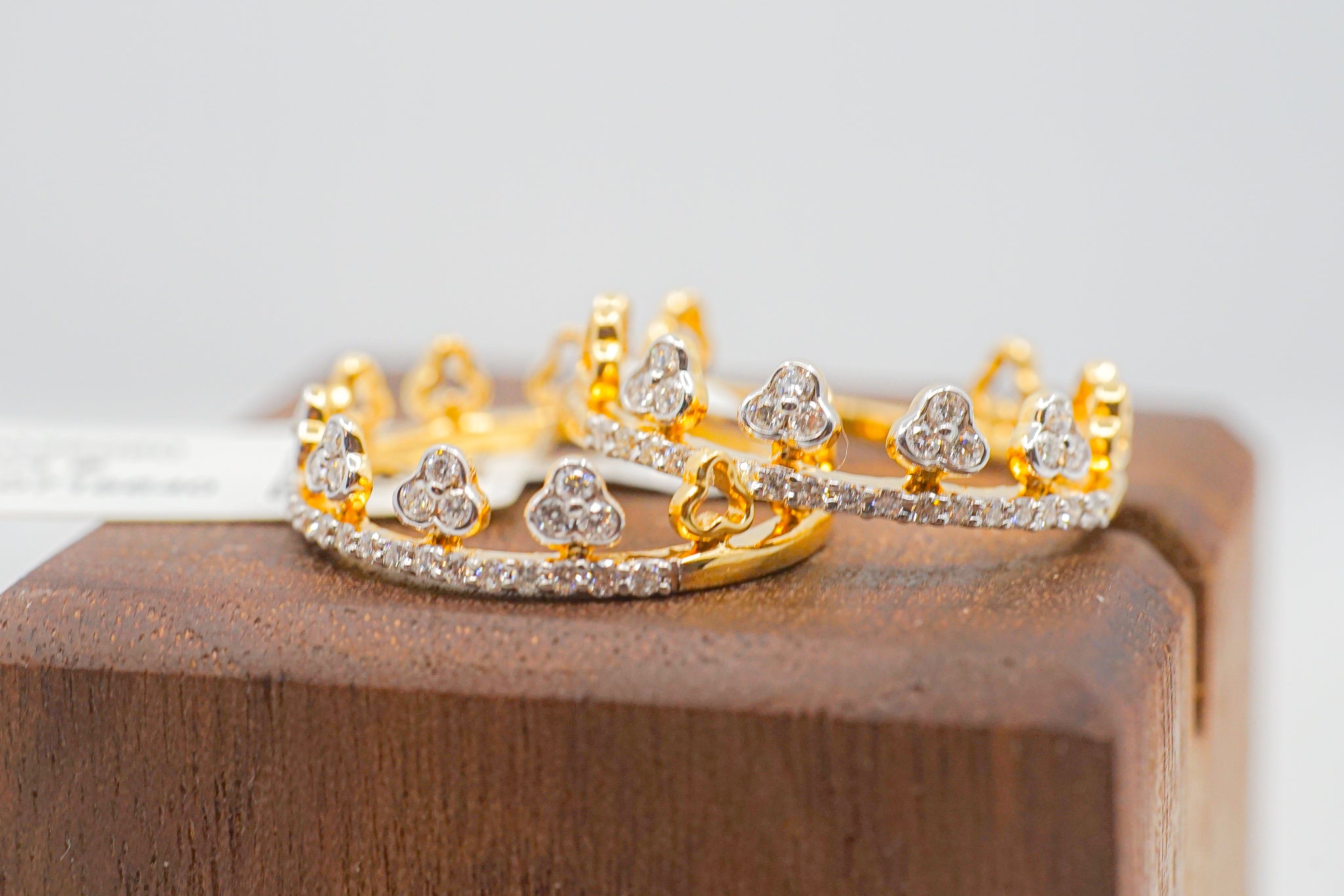 Two 18k gold crown band rings with diamond accents and heart-shaped motifs on a wooden display block