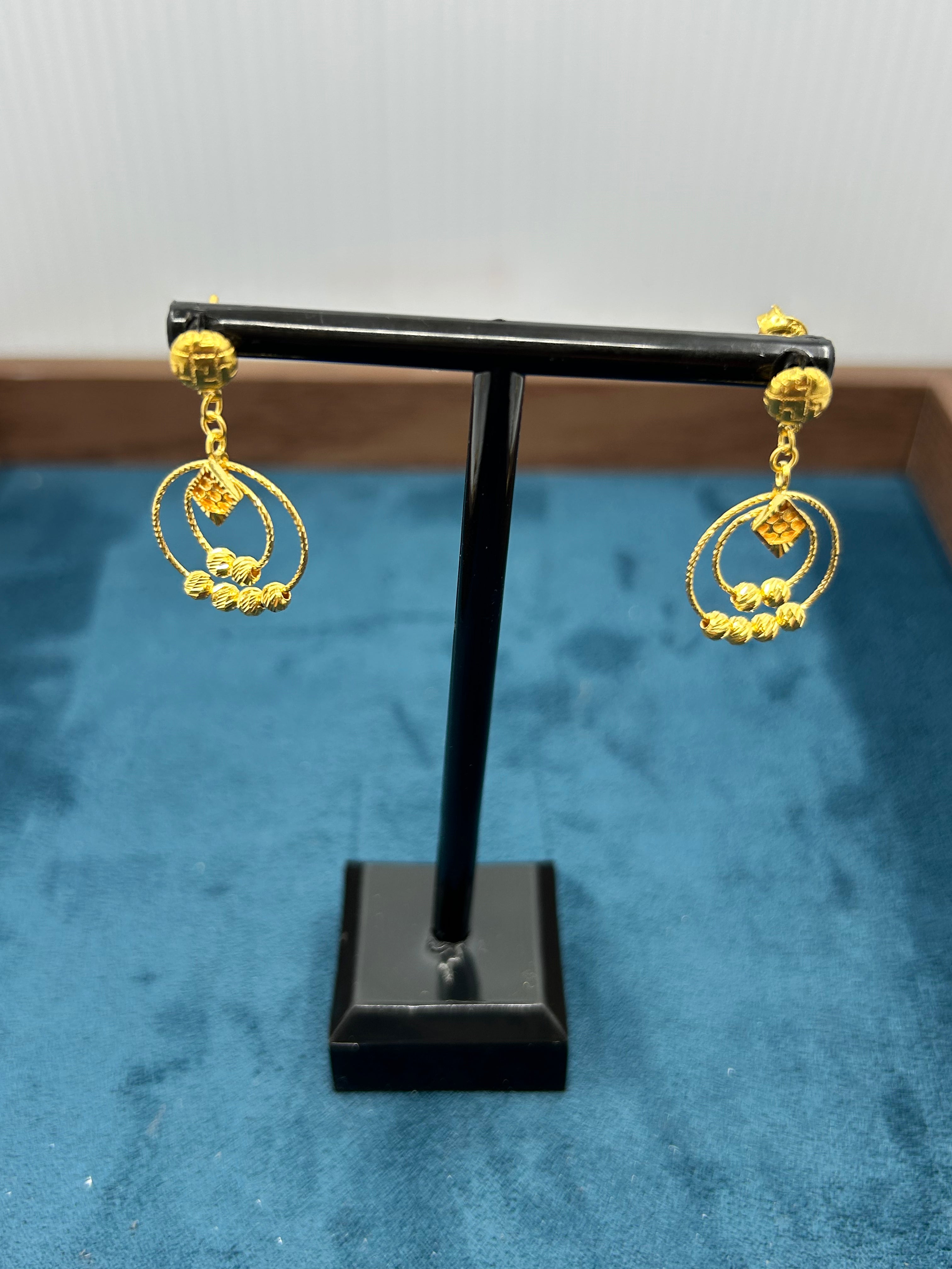 Gold earrings on a black stand against a blue background