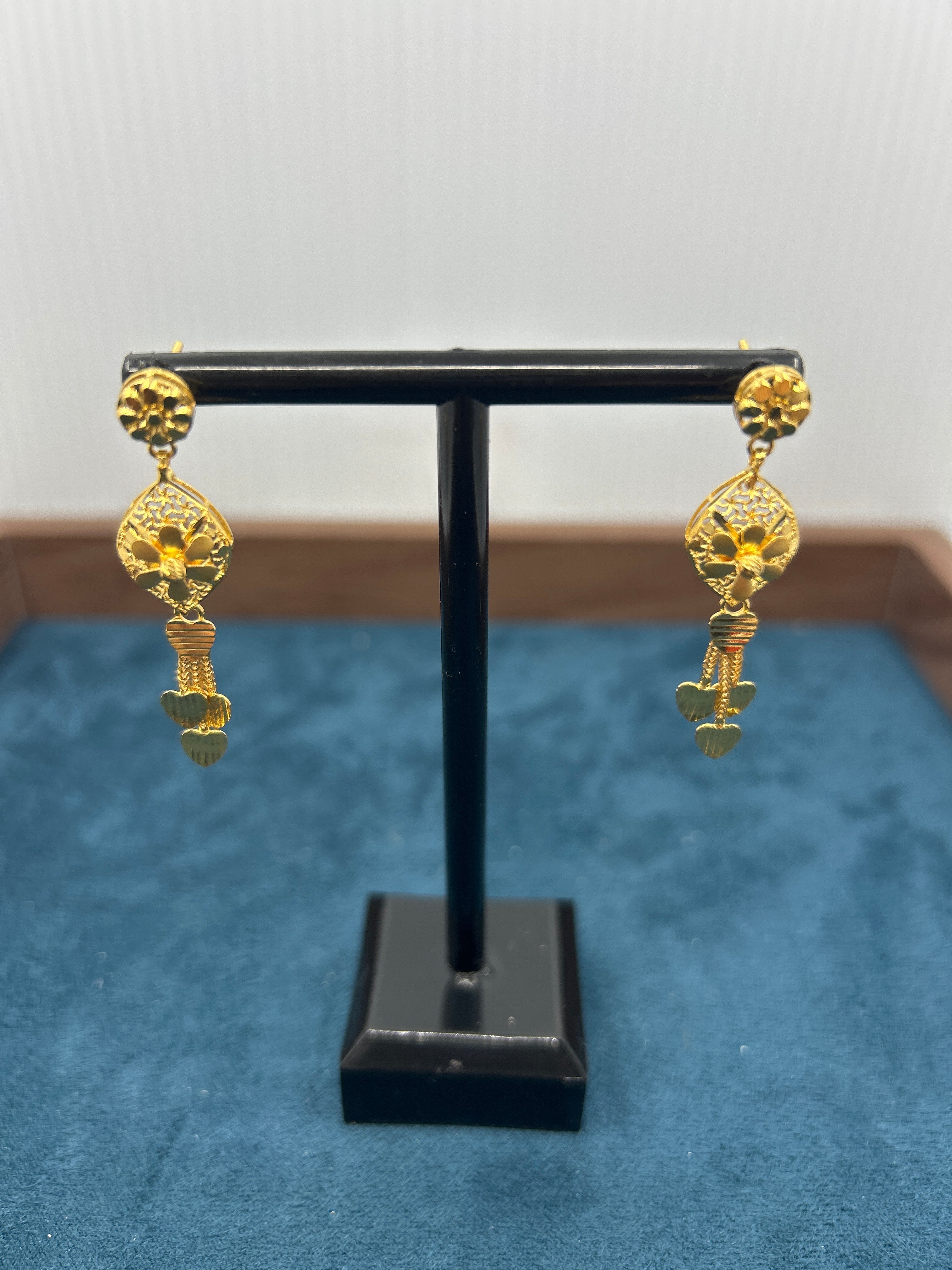 Pair of gold geometric drop dangle earrings on a black stand against a blue background.