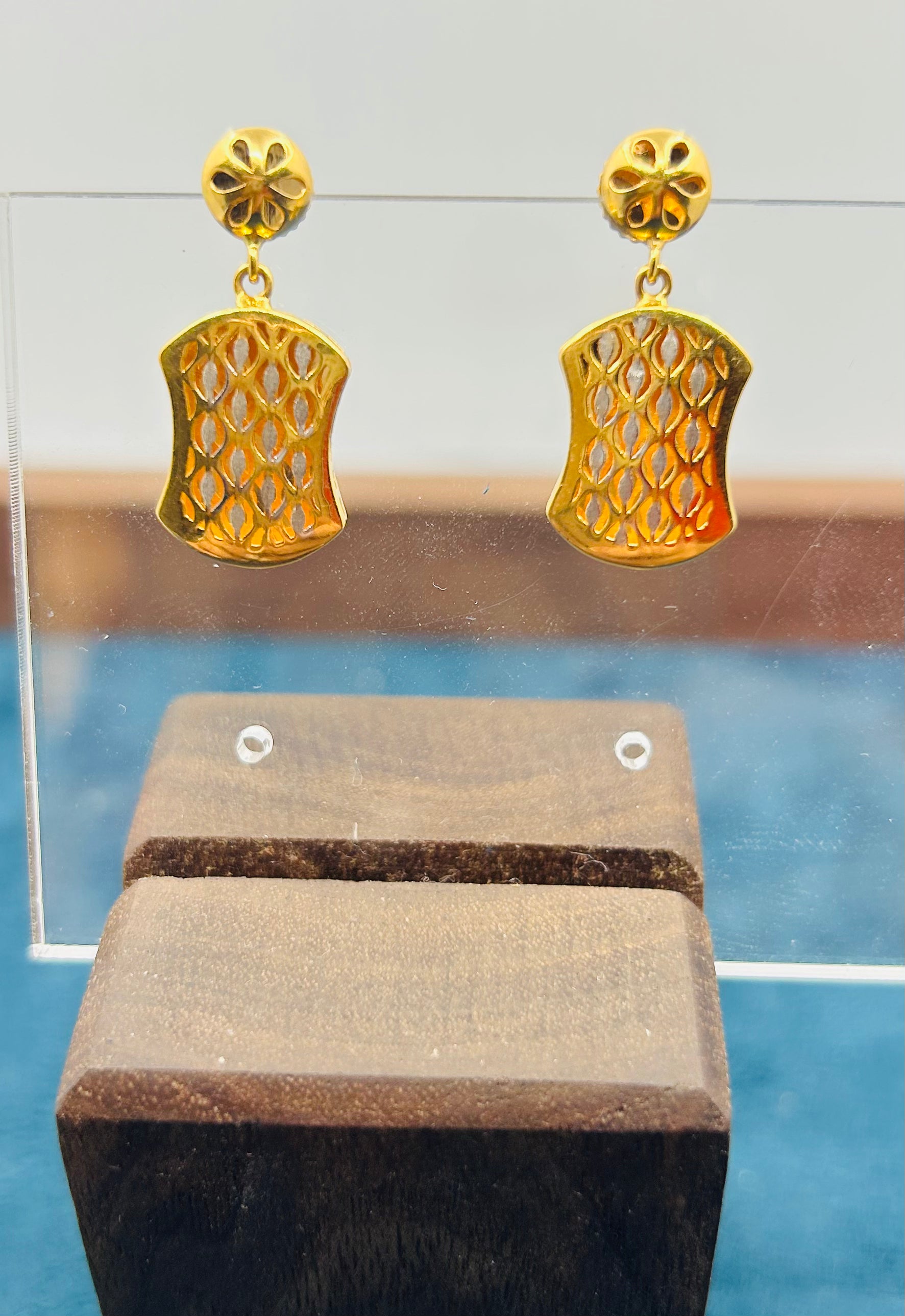 Gold lattice dangle earrings displayed on an earring stand