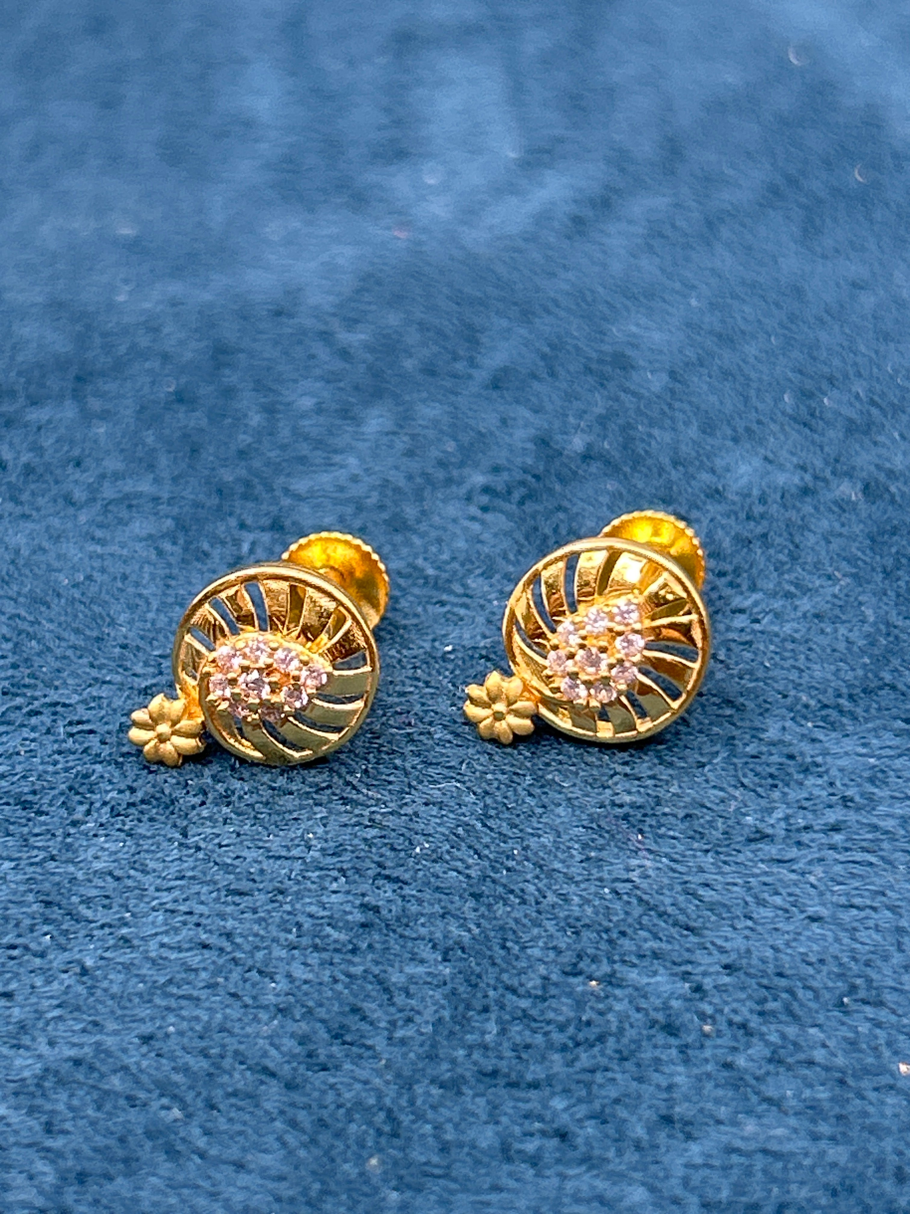 Pair of gold earrings with floral designs on a blue textured background